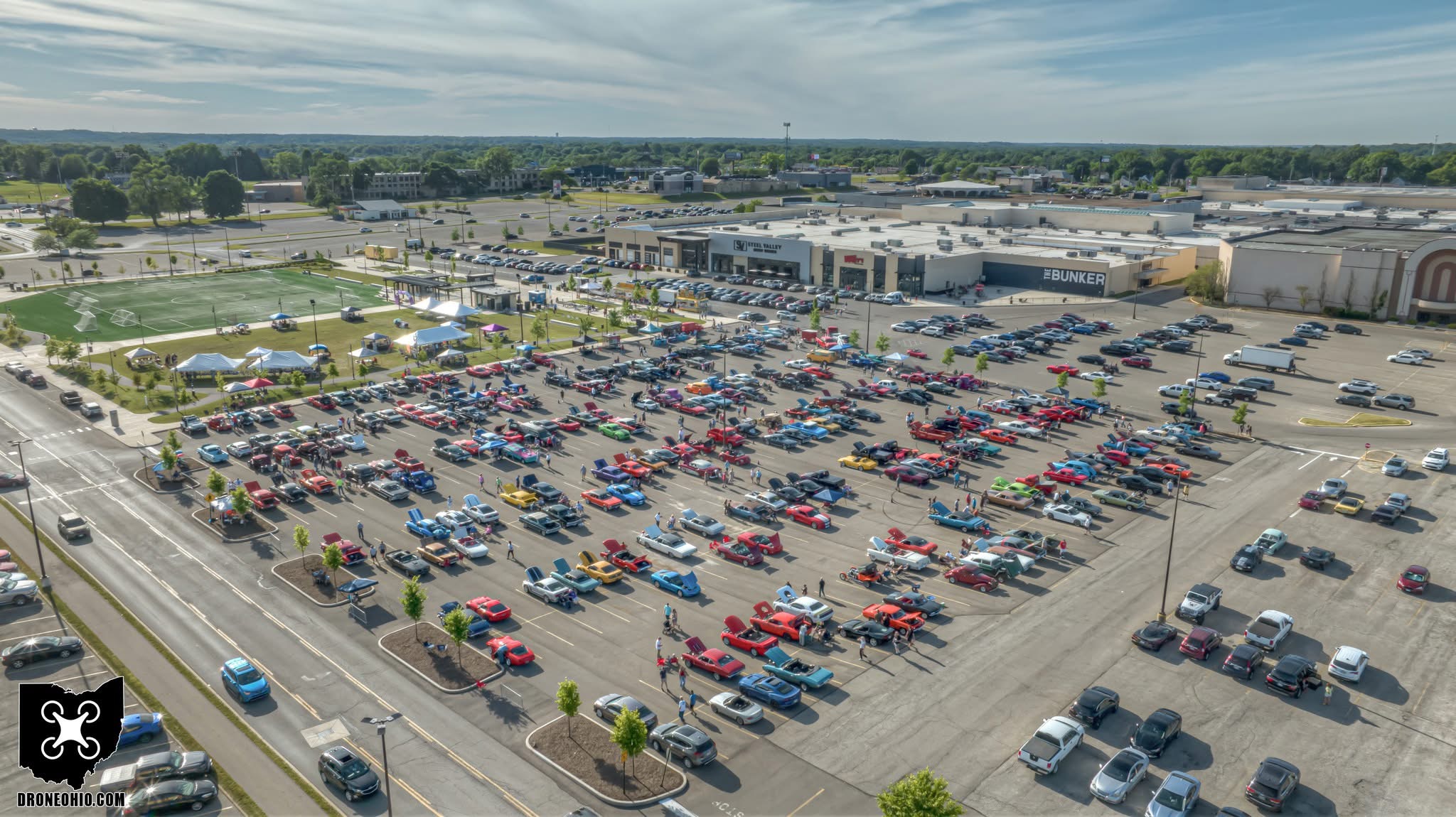 Large parking lot filled with cars outside a shopping mall, with a road and trees in the background.