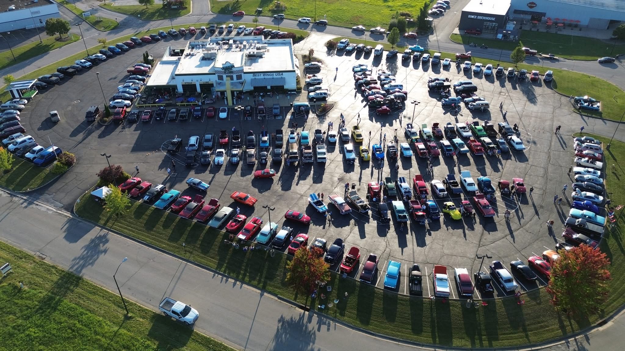 Aerial view of a large parking lot filled with cars, adjacent to a building, with surrounding greenery and trees.