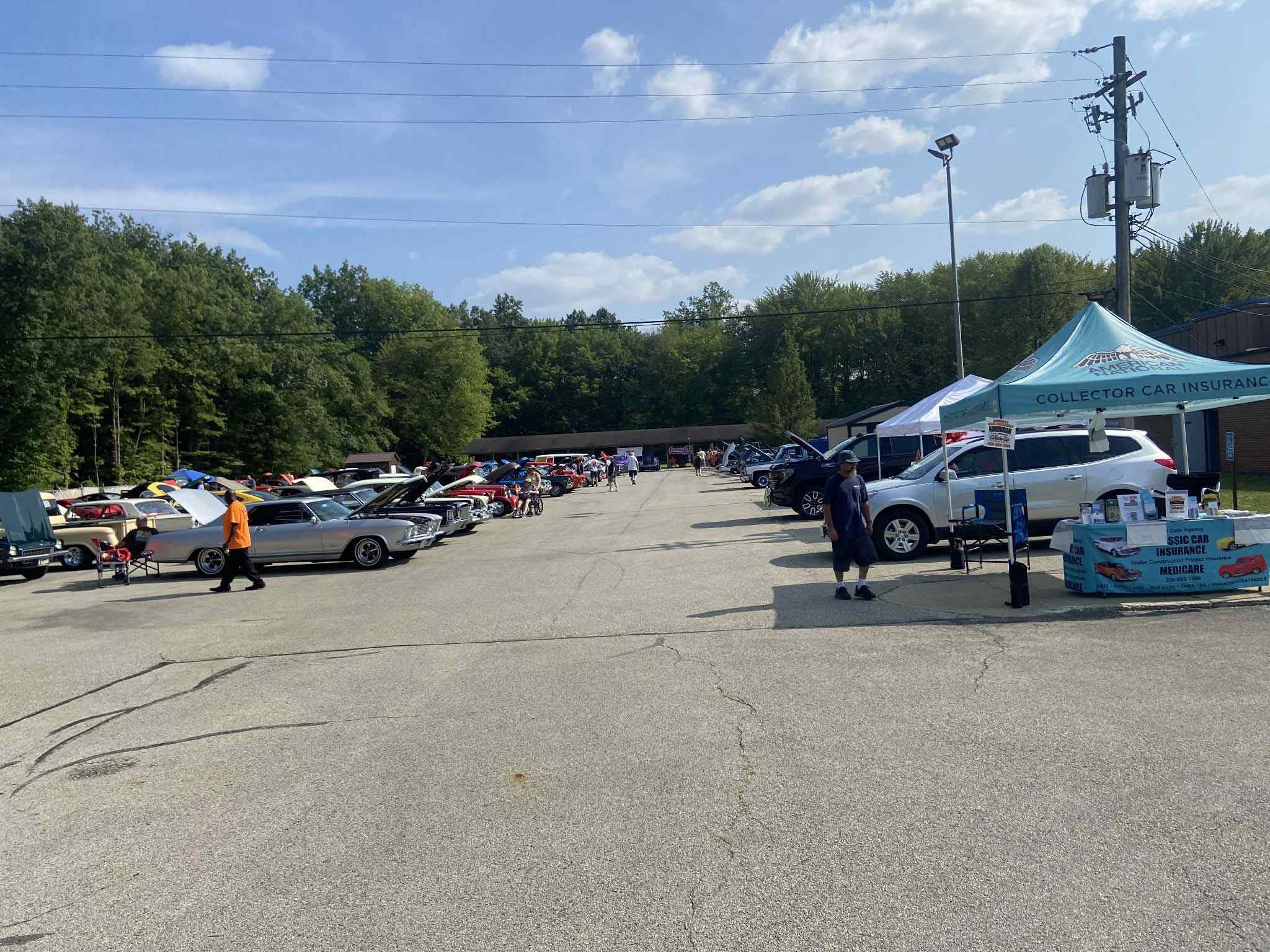 Parking lot with cars, a tent, and trees in the background under a partly cloudy sky.