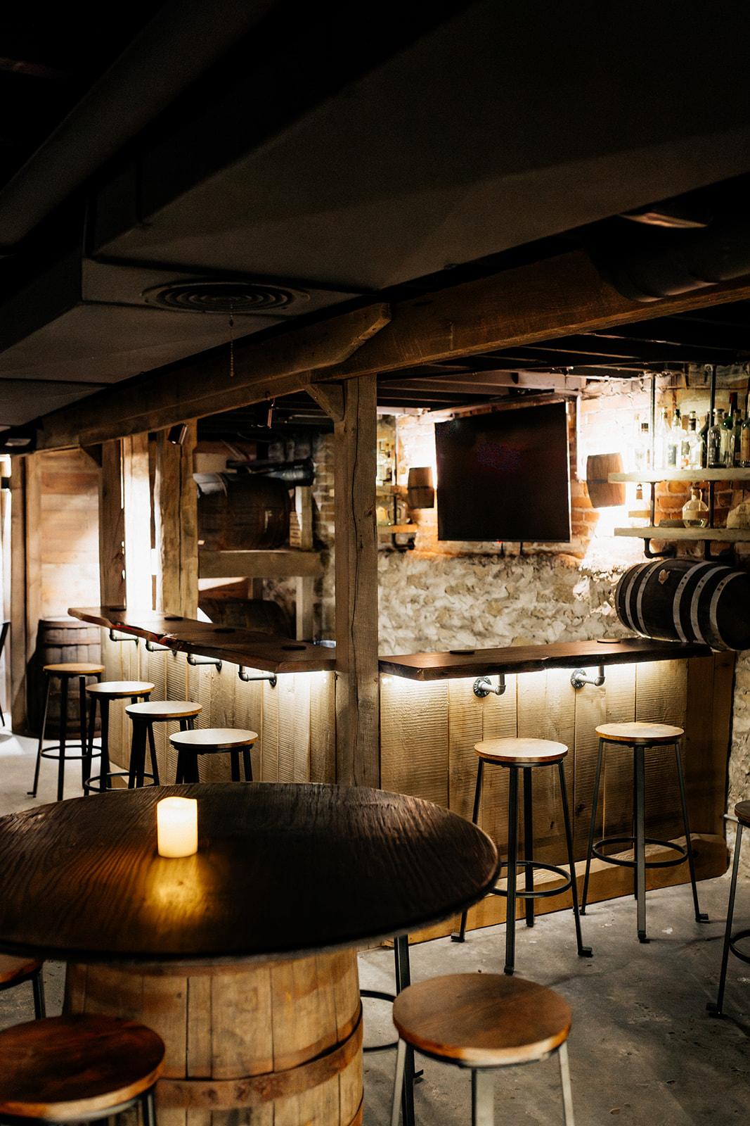 Interior of a bar with a wooden counter, bar stools, and a small lit candle on a round table, dim lighting.