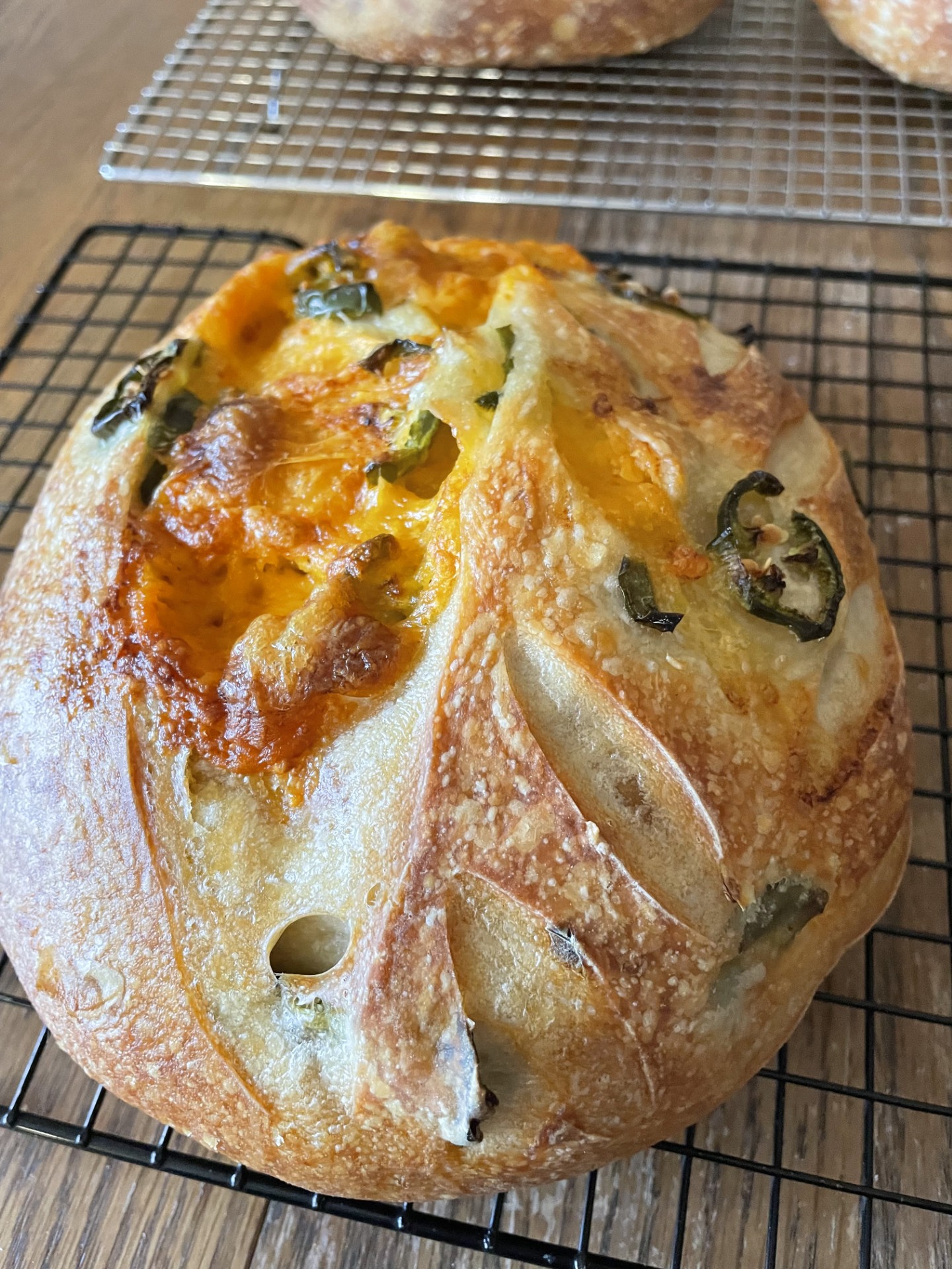 Round bread with melted cheese, green herbs, and sliced vegetables on top, cooling on a wire rack.