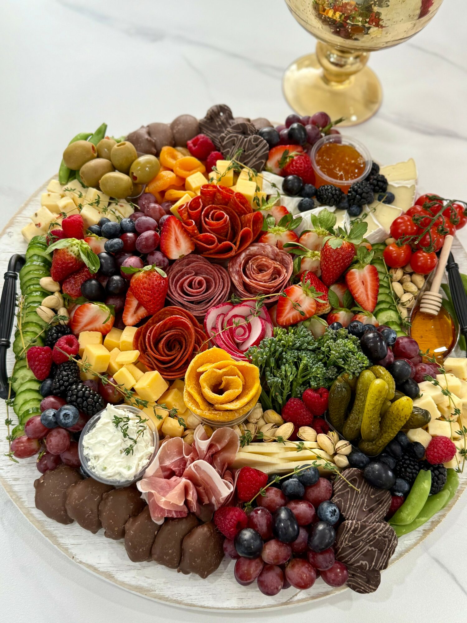 Colorful fruit and chocolate cake with strawberries, blueberries, grapes, and decorative roses, on a white surface with a glass of wine.