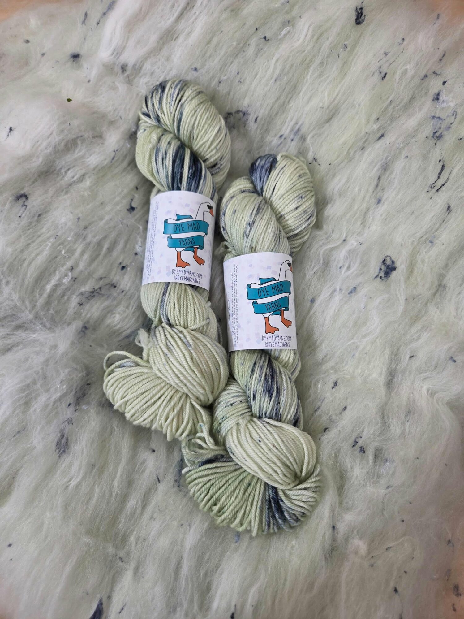 Two skeins of yarn with labels featuring a blue robot, placed on a light-colored furry surface.