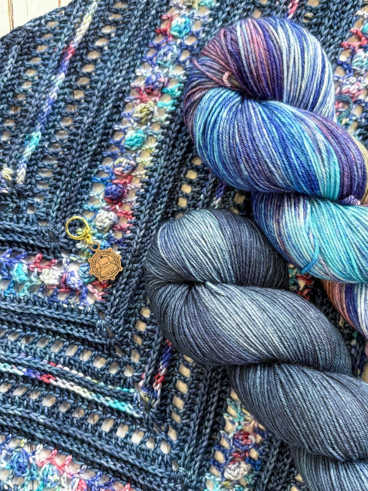 Colorful yarn skeins placed on a textured, multicolored woven fabric background.