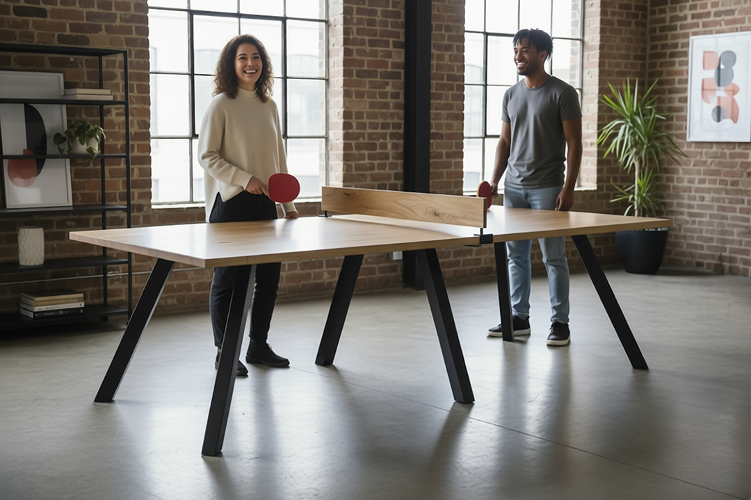 Two people playing table tennis in a spacious room with large windows and brick walls.