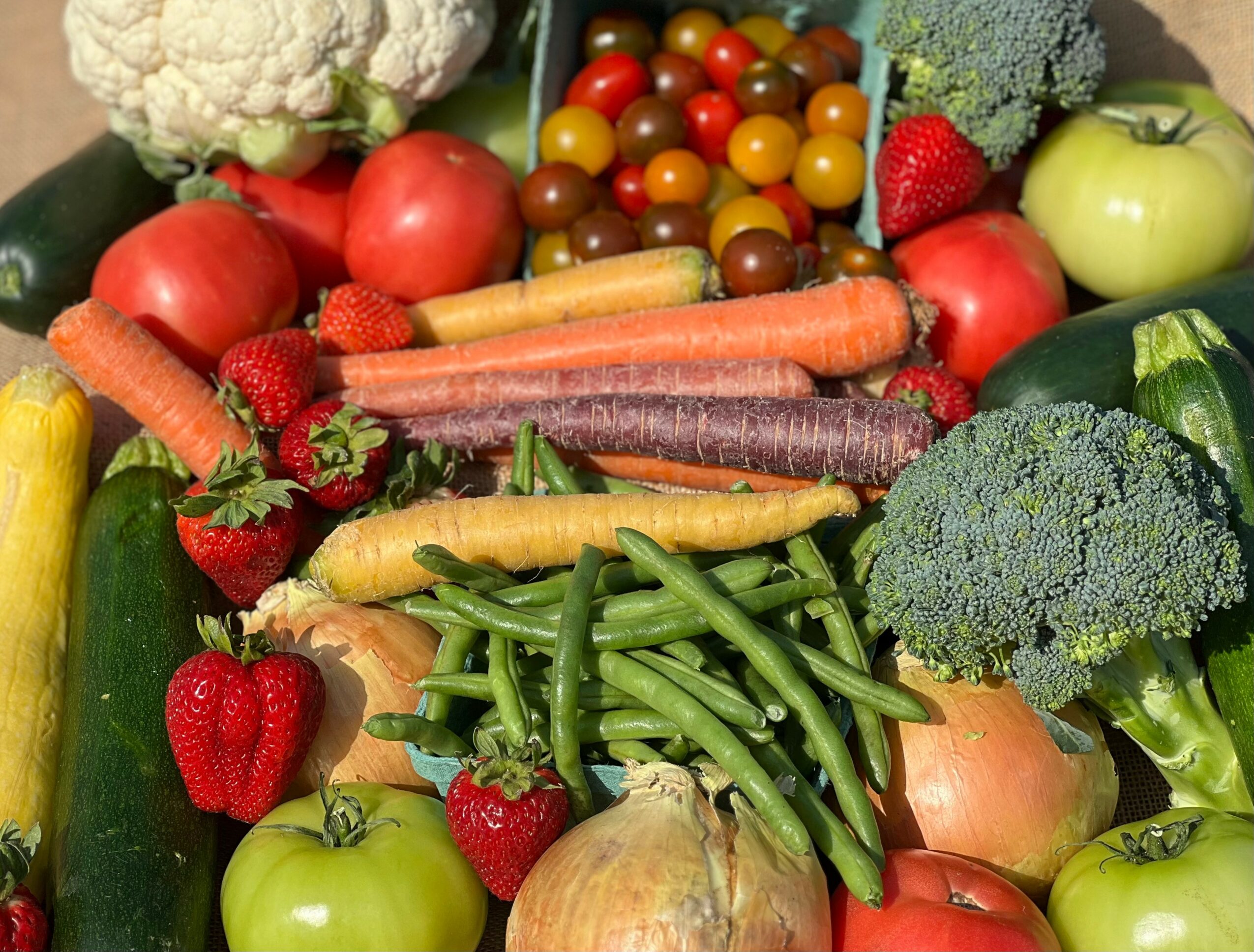 Assorted fresh vegetables and fruits including broccoli, carrots, strawberries, apples, cauliflower, cherry tomatoes, and zucchini.