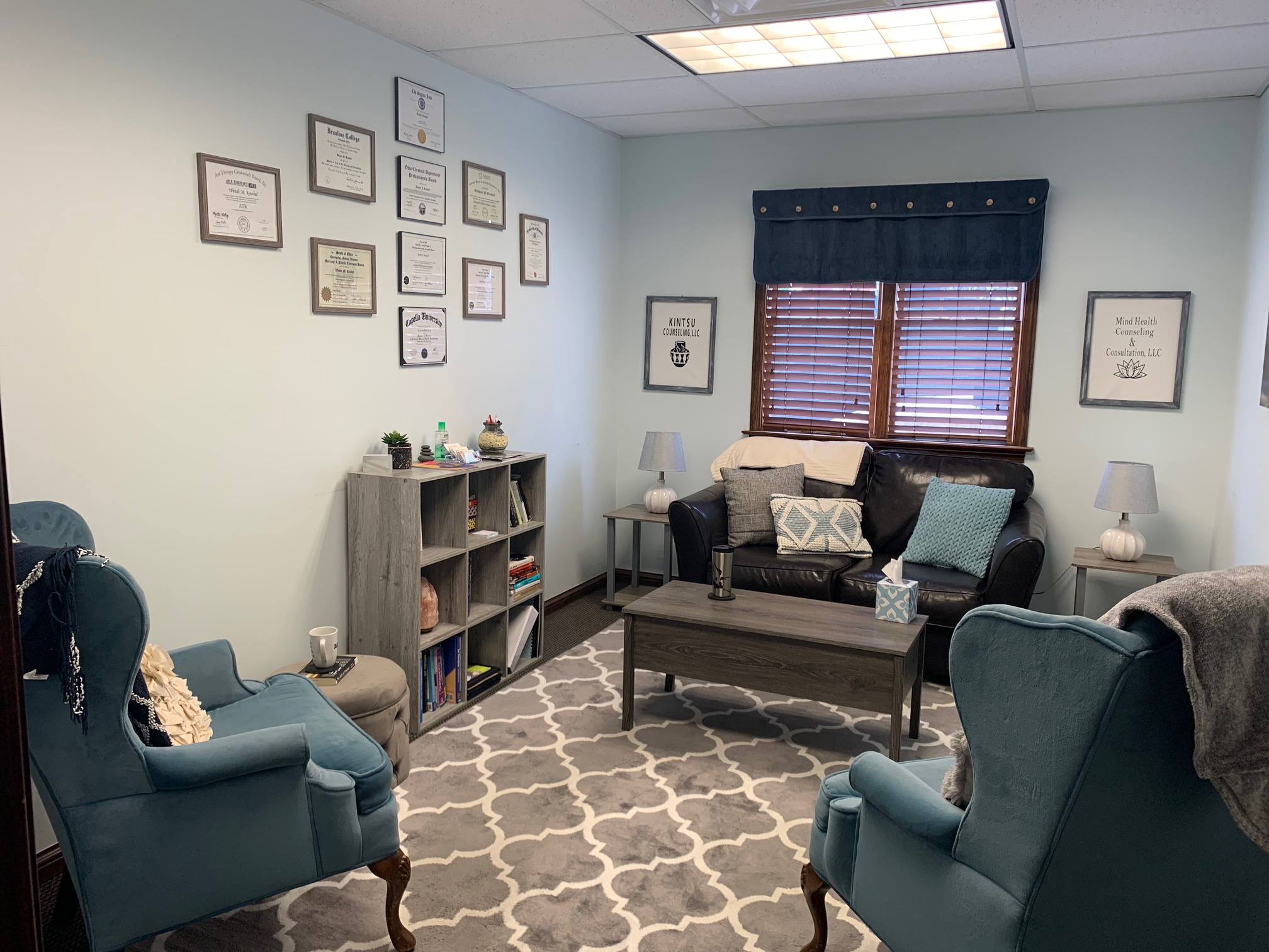 Living room with two blue armchairs, a gray sofa, a patterned rug, and framed pictures on light blue walls.