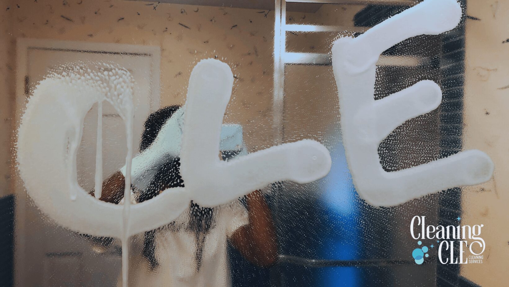 Frosted word 'CLEAN' written on a glass surface with a person taking a photo in the background.