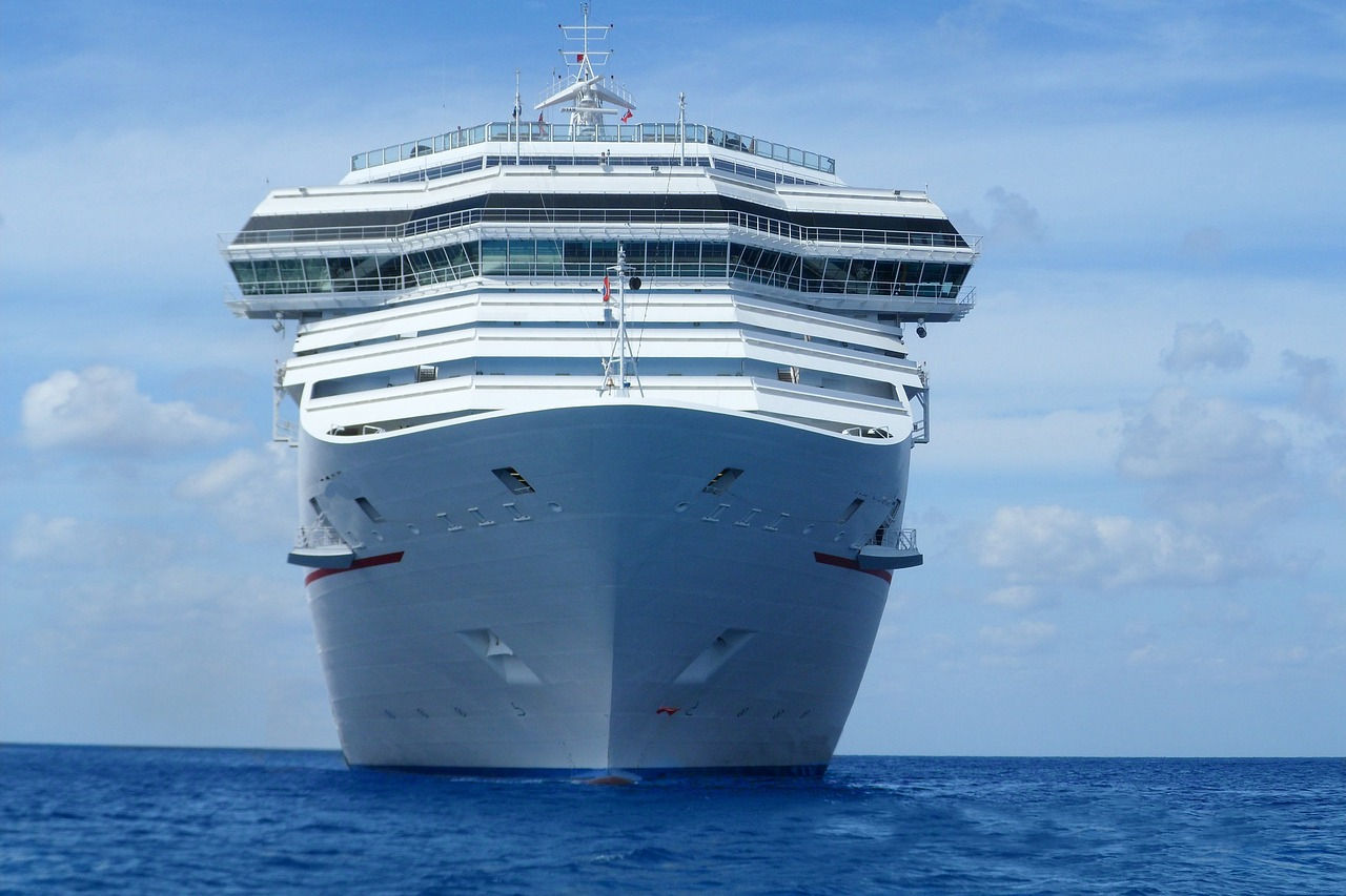 Large cruise ship on the ocean with a blue sky and clouds above, viewed from the front.