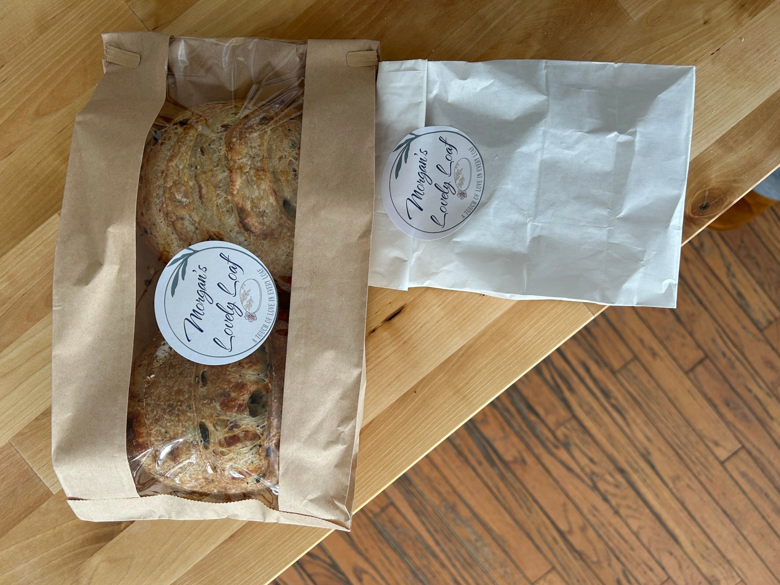 Two paper bags, one transparent with baked goods, on a wooden surface.