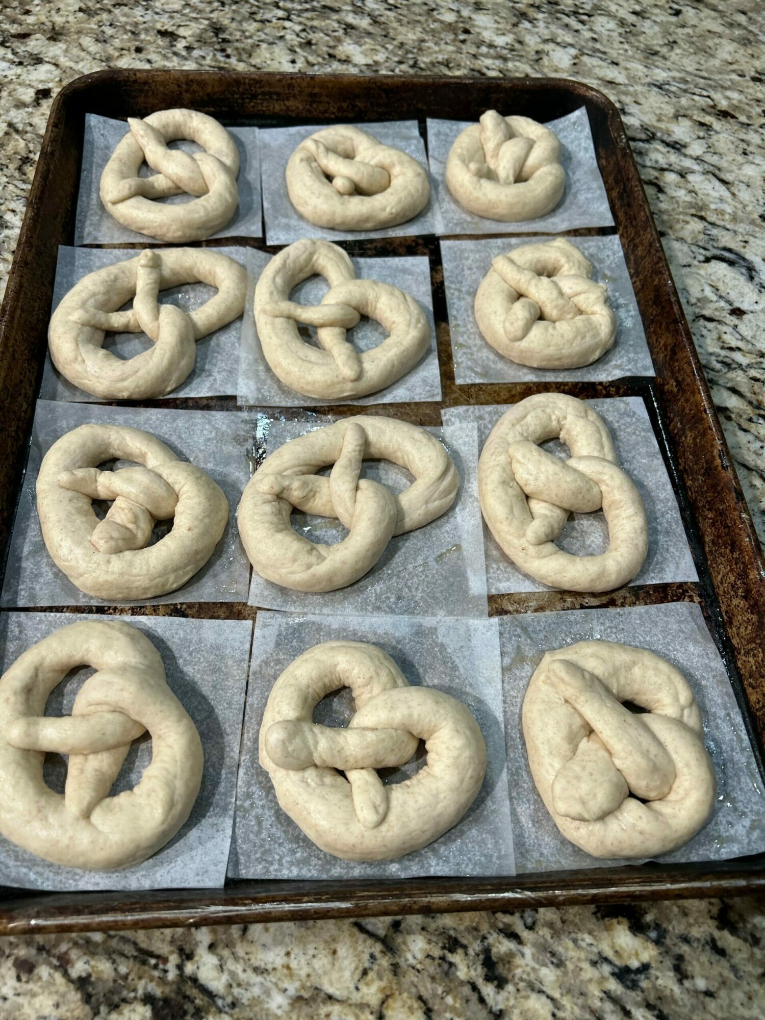 Tray of unbaked pretzels on parchment paper, arranged in three rows, with some pretzels having a small dark spot.