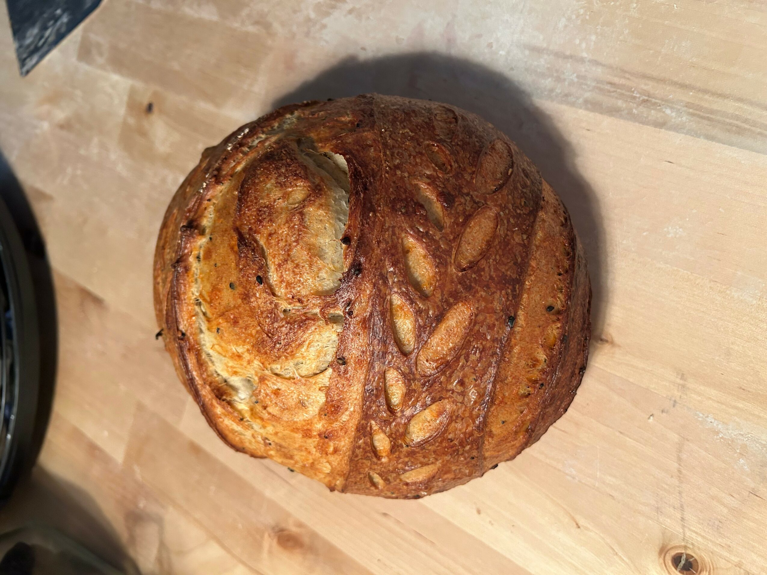 Round loaf of bread with a decorative pattern on top, placed on a wooden surface.