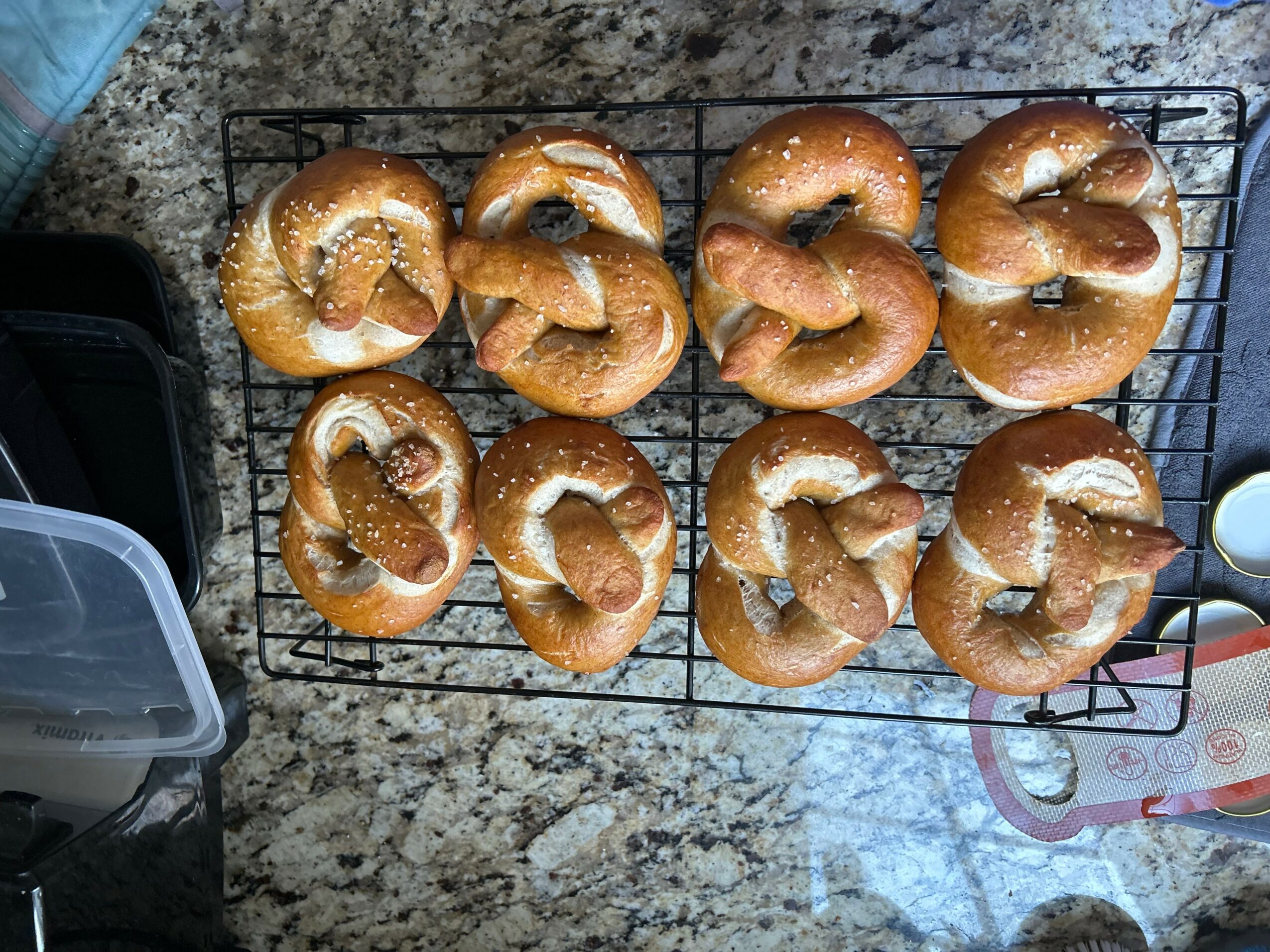 Eight bagels with cream cheese on a wire rack on a granite countertop.