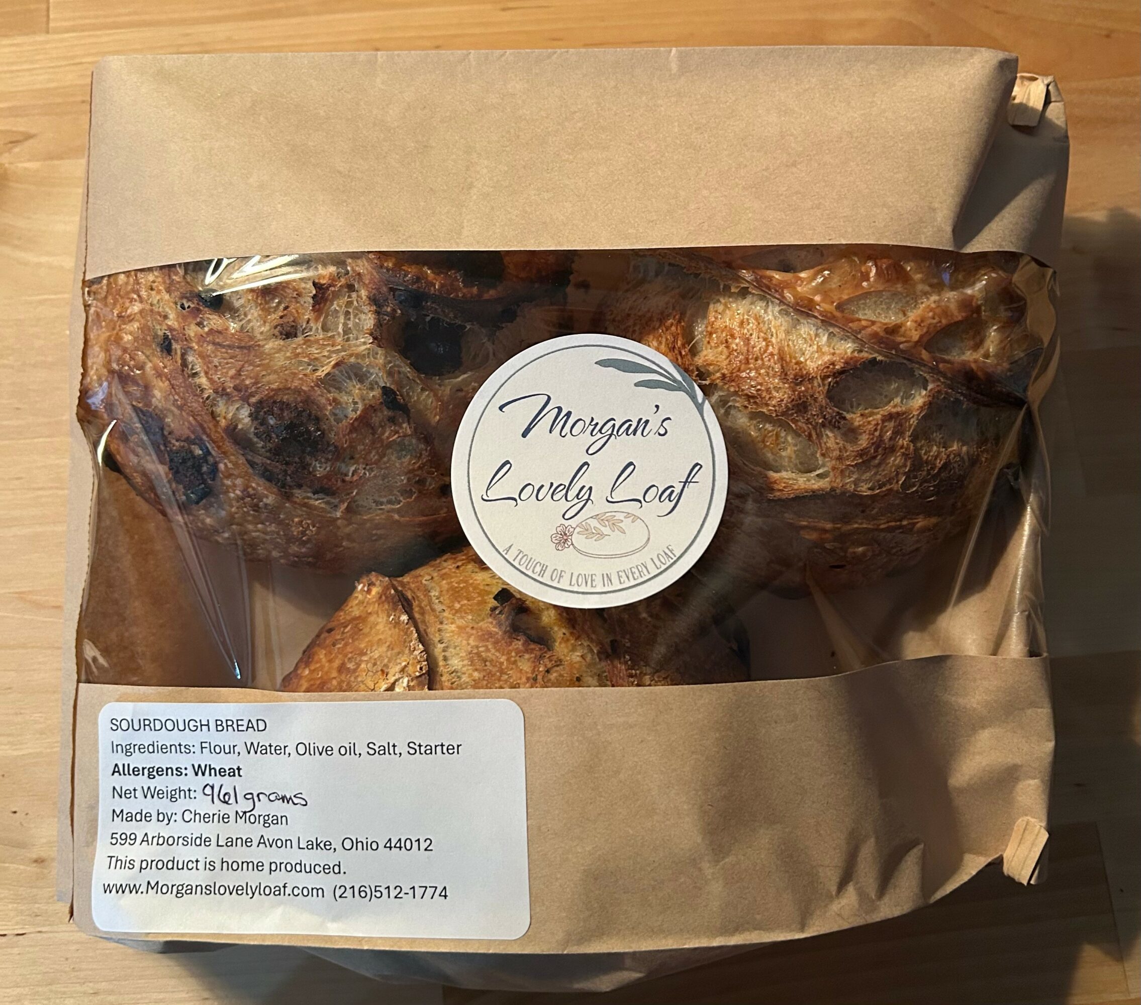 Sourdough bread in clear plastic bag with label, ingredients, allergens, and website information visible.