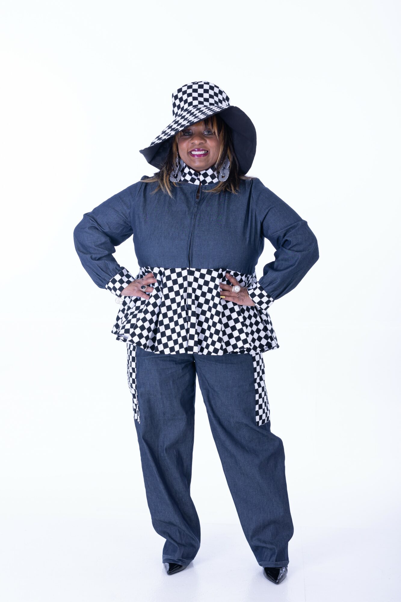 Child wearing a denim jacket, checkered hat, and matching checkered pattern on jacket and pants, smiling with hands on hips.