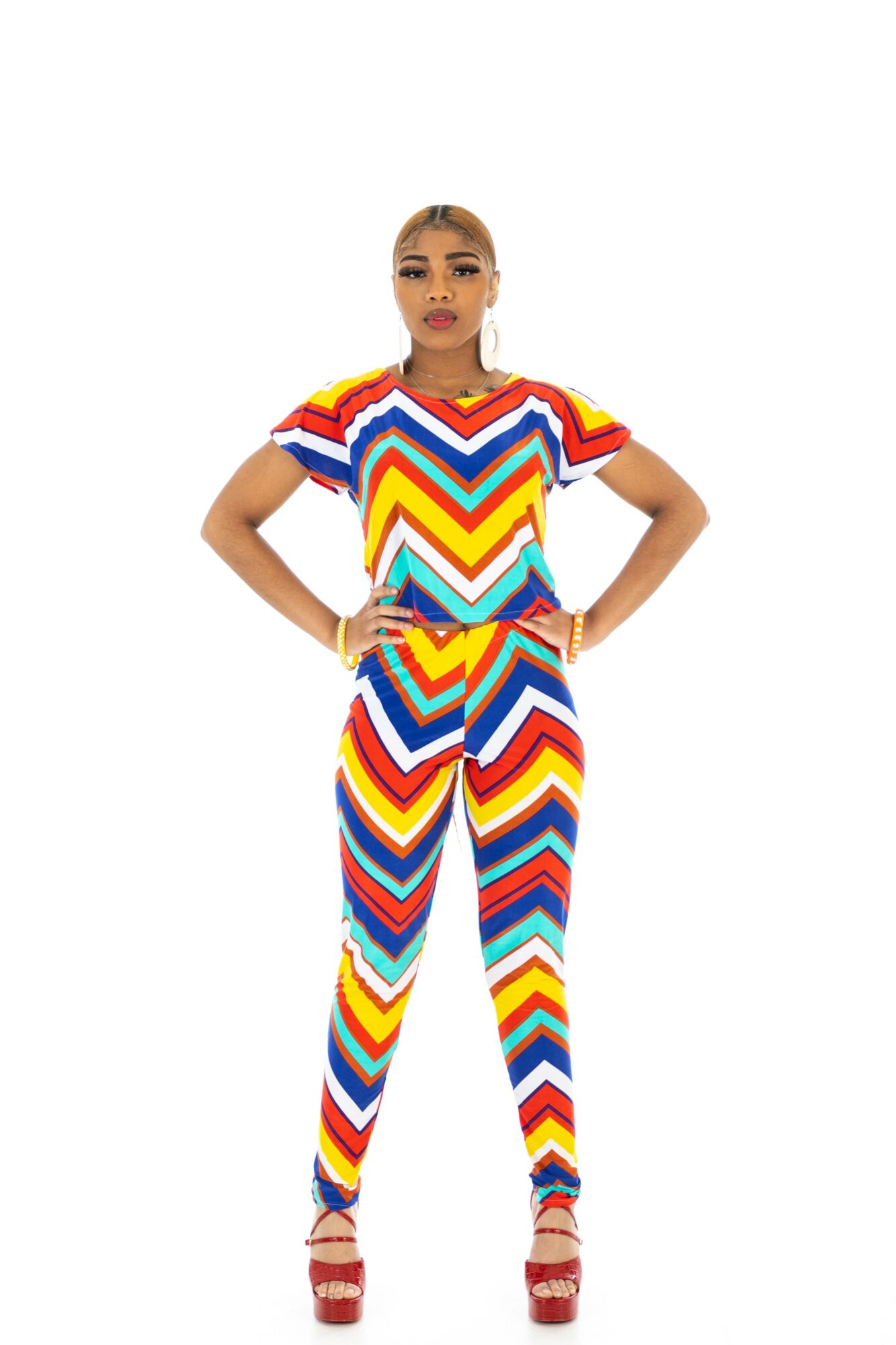 Woman in colorful zigzag patterned outfit with hands on hips, standing against white background.