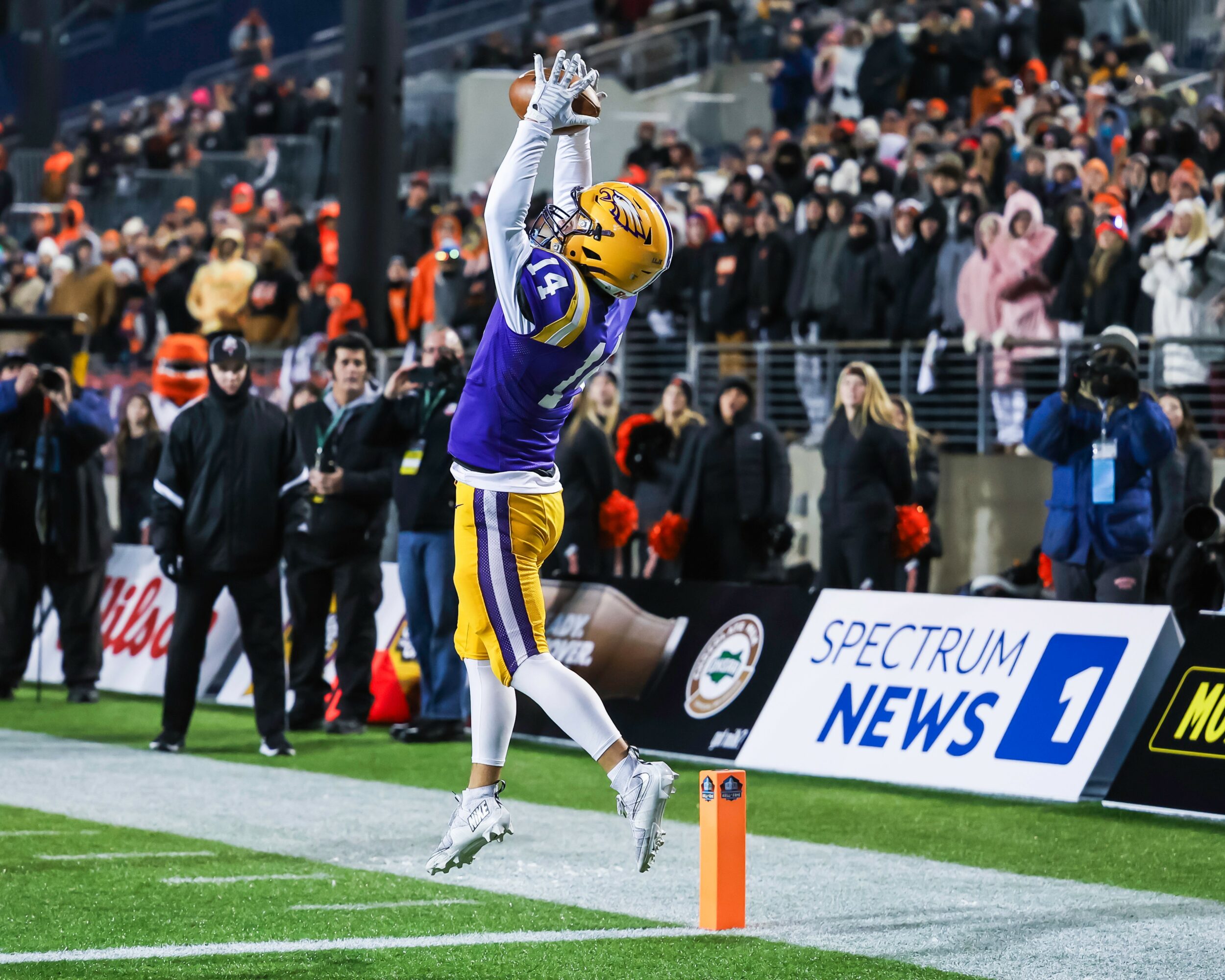Football player in purple and yellow uniform celebrating in end zone with crowd in background.