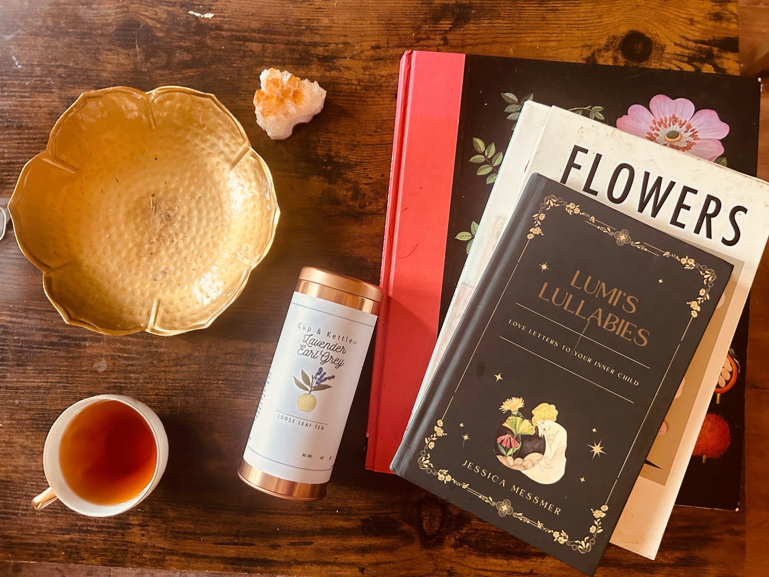 Golden bowl, small flower, tea cup, and books on a wooden surface.