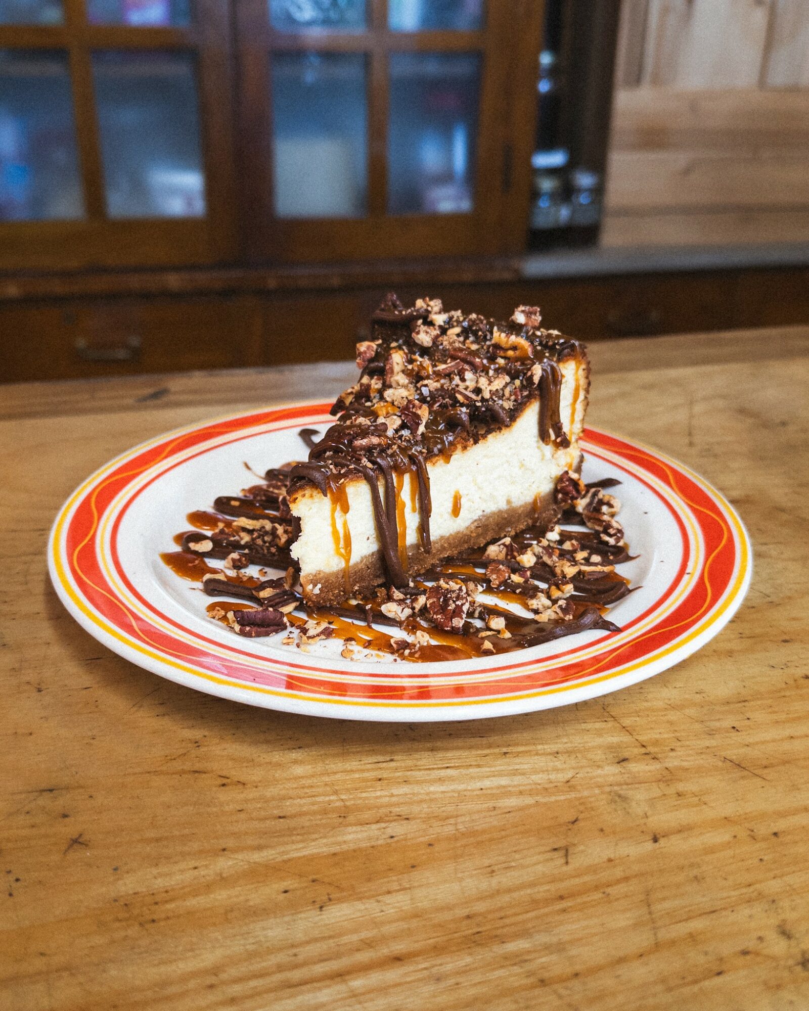 Cheesecake with caramel, chocolate, and nut toppings on a colorful plate, on a wooden table.