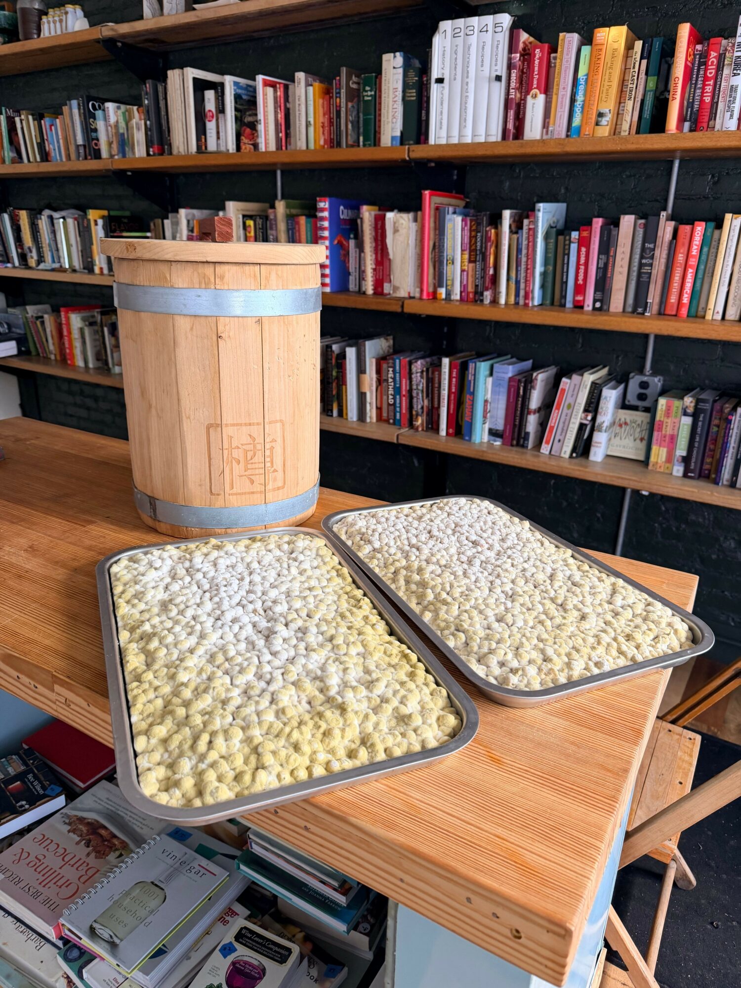 Two metal containers filled with popcorn on a wooden table, with bookshelves in the background.