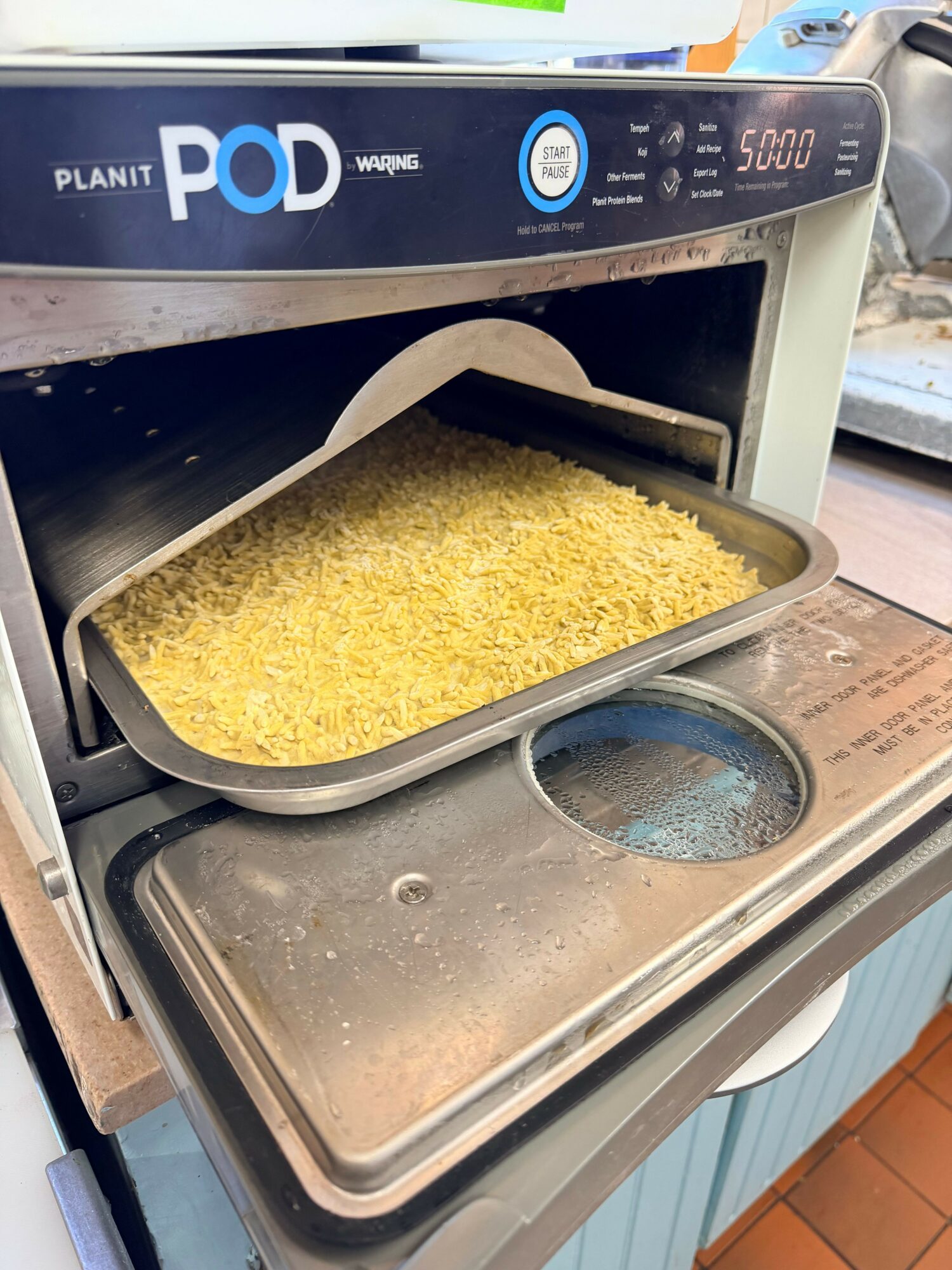 A rice cooker with a yellow rice dish inside, partially covered, on a kitchen counter.