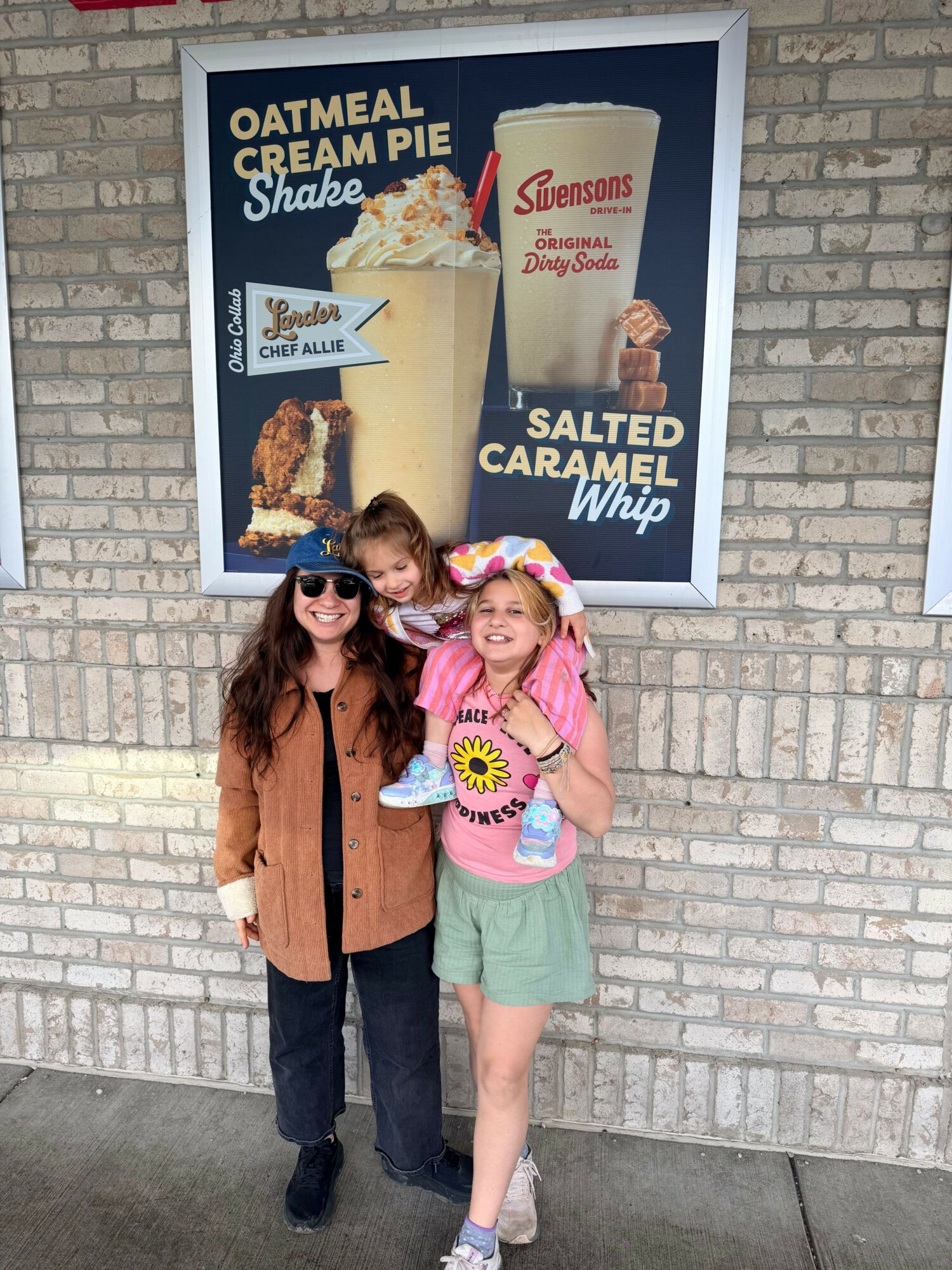 Two women stand outside a brick building next to a sign for a show, smiling and posing for the photo.
