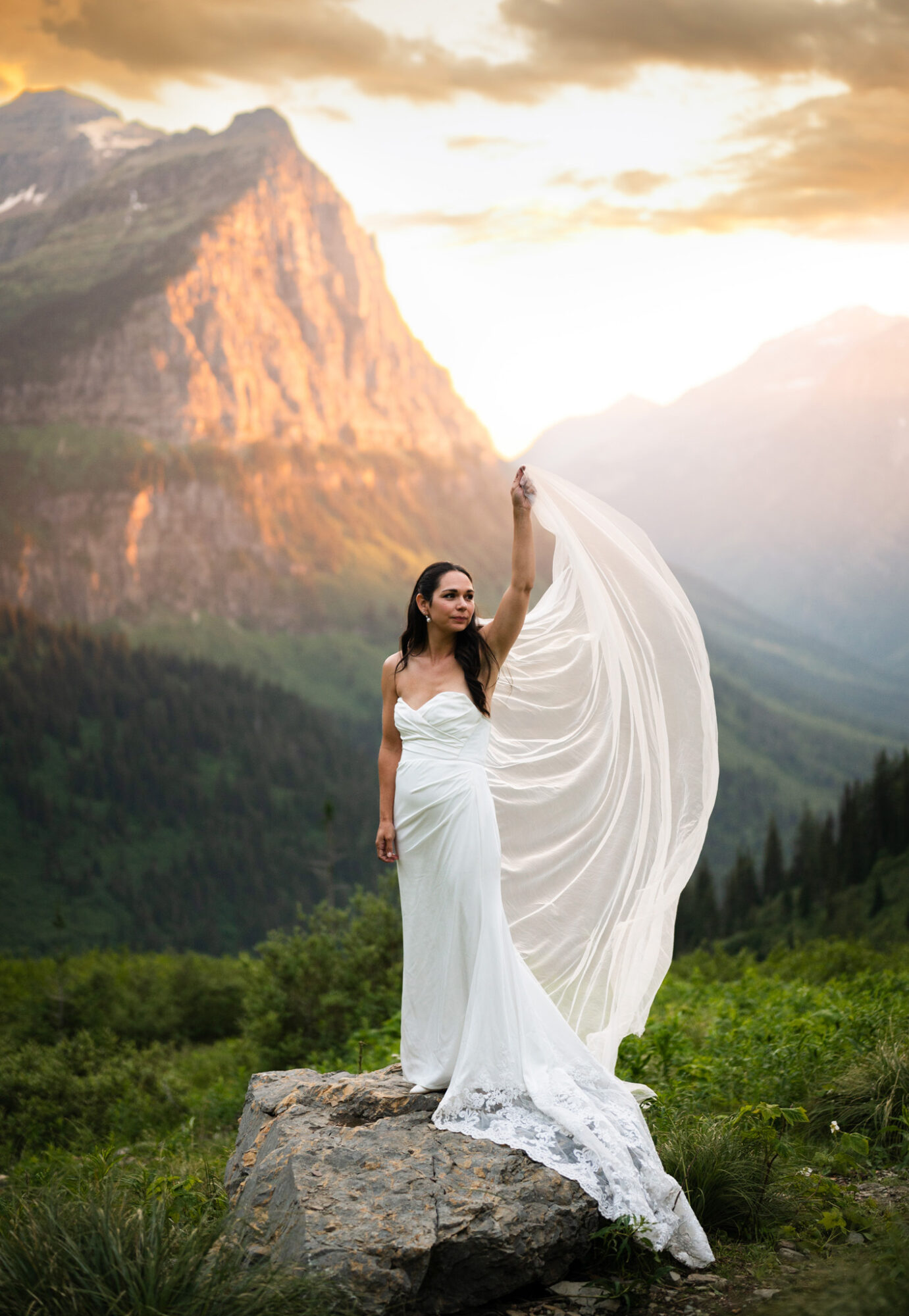 Woman in a white dress standing on a rock in a mountain landscape with a flowing veil, mountains in the background