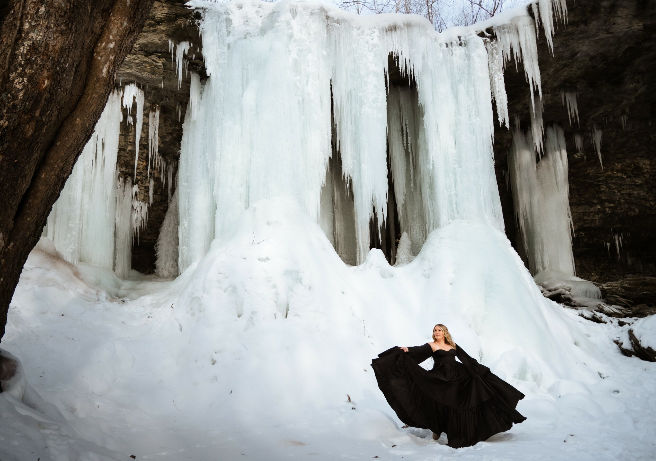 Person in black dress sitting in front of frozen waterfall with icicles and ice formations.