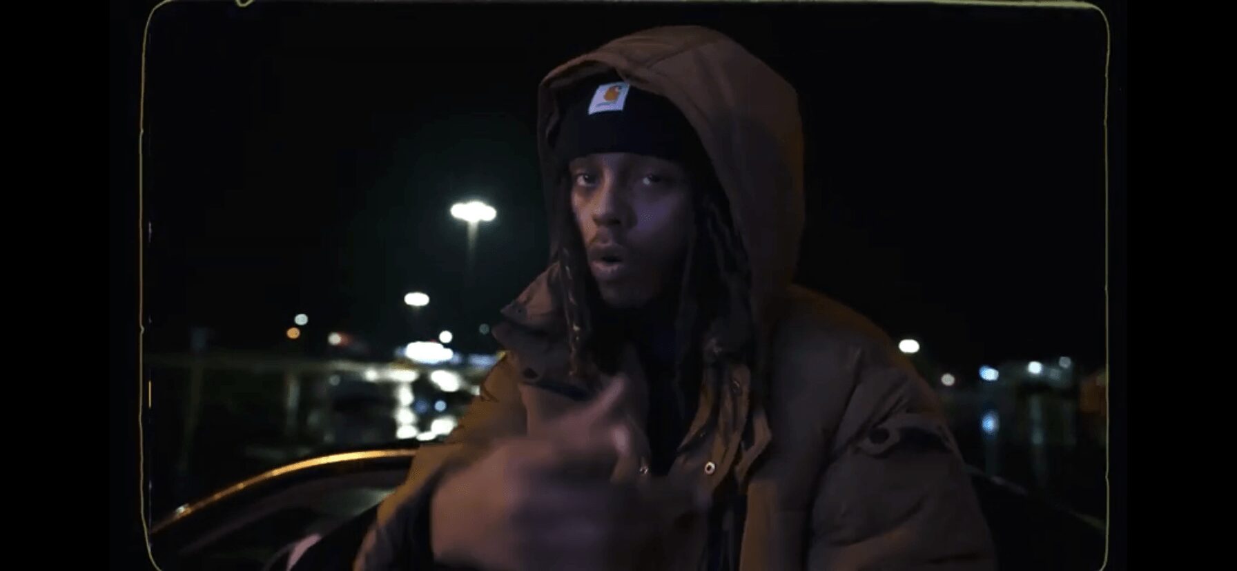 Person wearing a hooded jacket outdoors at night, with city lights in the background.
