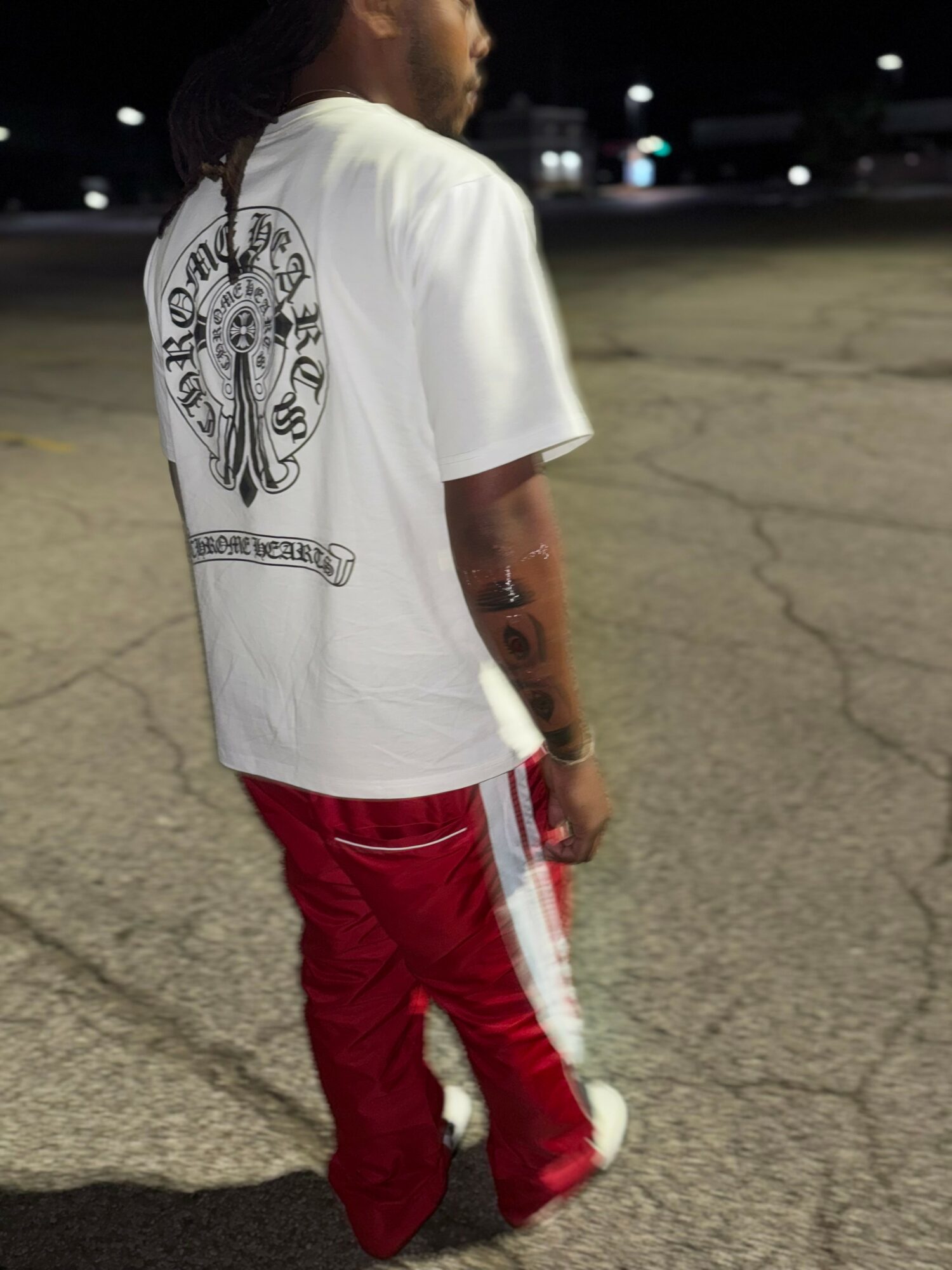 Person standing outdoors at night, wearing a white T-shirt with a graphic on the back and red pants with white stripes.