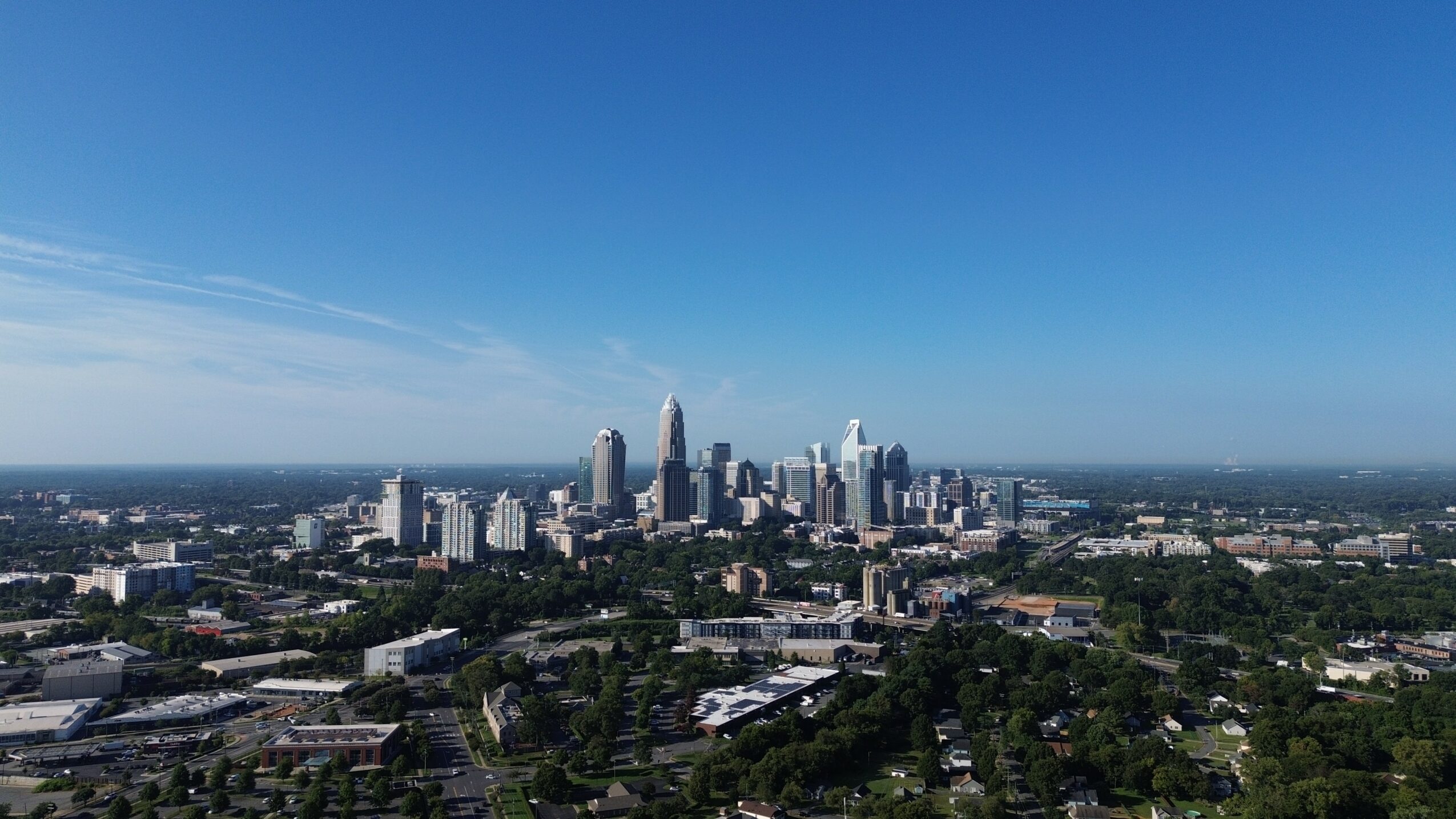 City skyline with tall buildings under a clear blue sky, surrounded by greenery and low-rise structures.