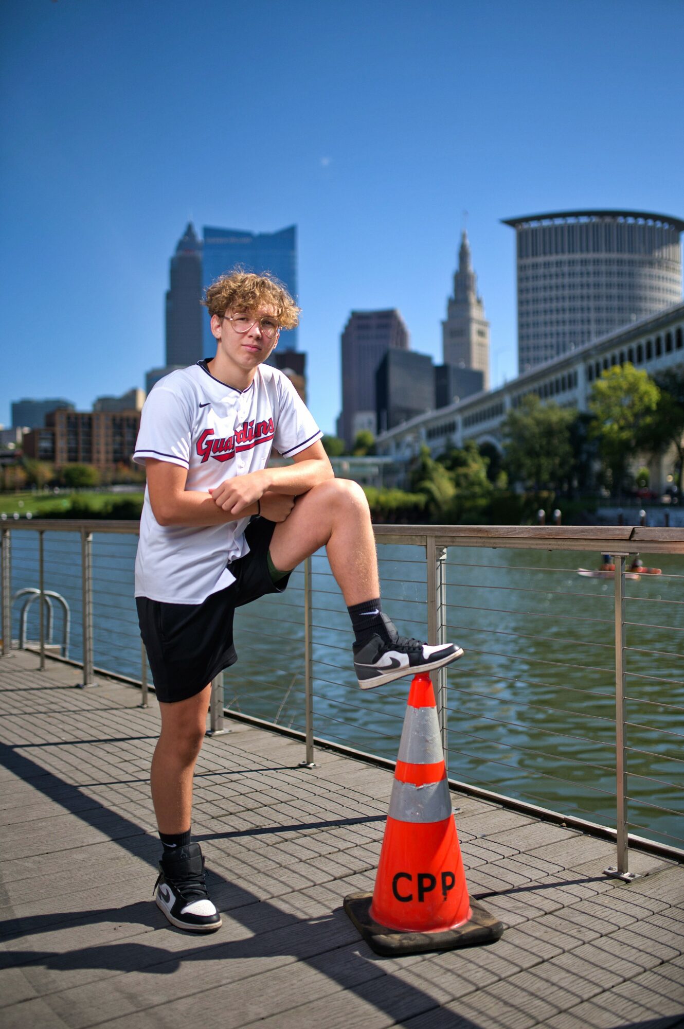 Young person with curly hair stretching on a waterfront promenade with city skyline in background.