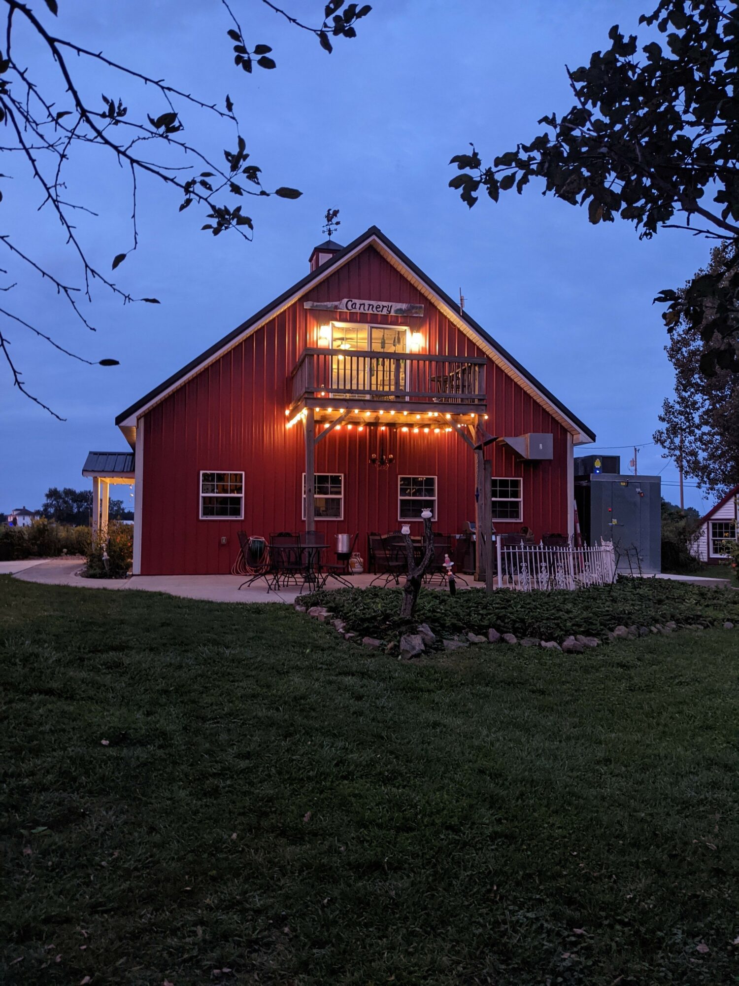 Red house with illuminated windows and porch, surrounded by grass and trees, during evening or dusk.