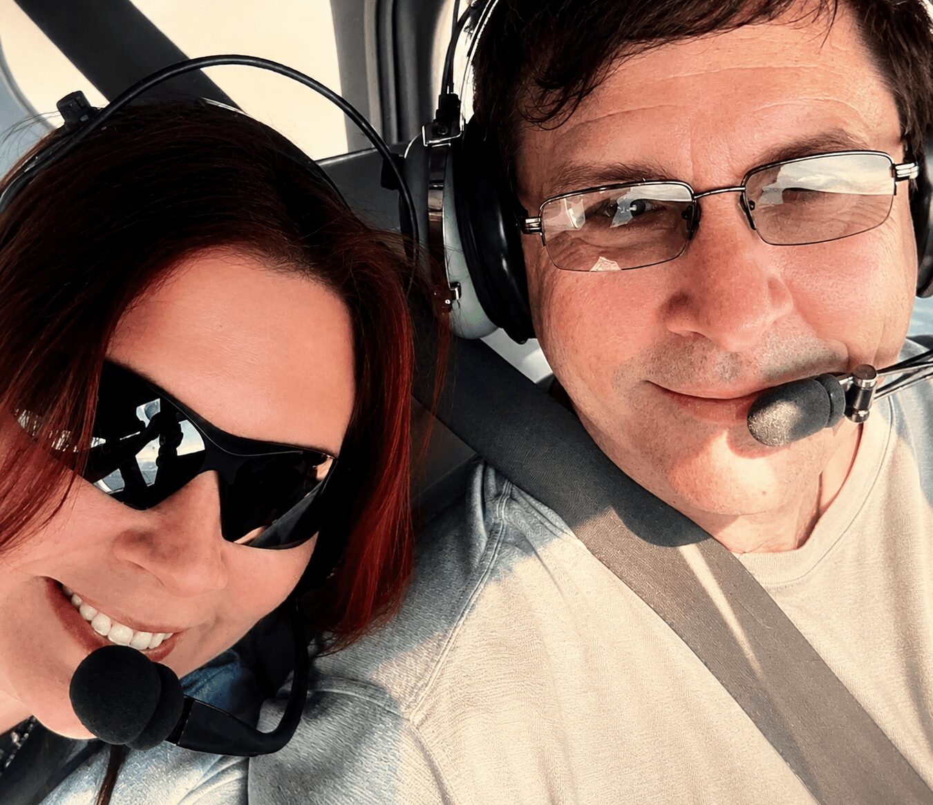 Two people wearing headsets with microphones, smiling, close-up, inside an aircraft cockpit.