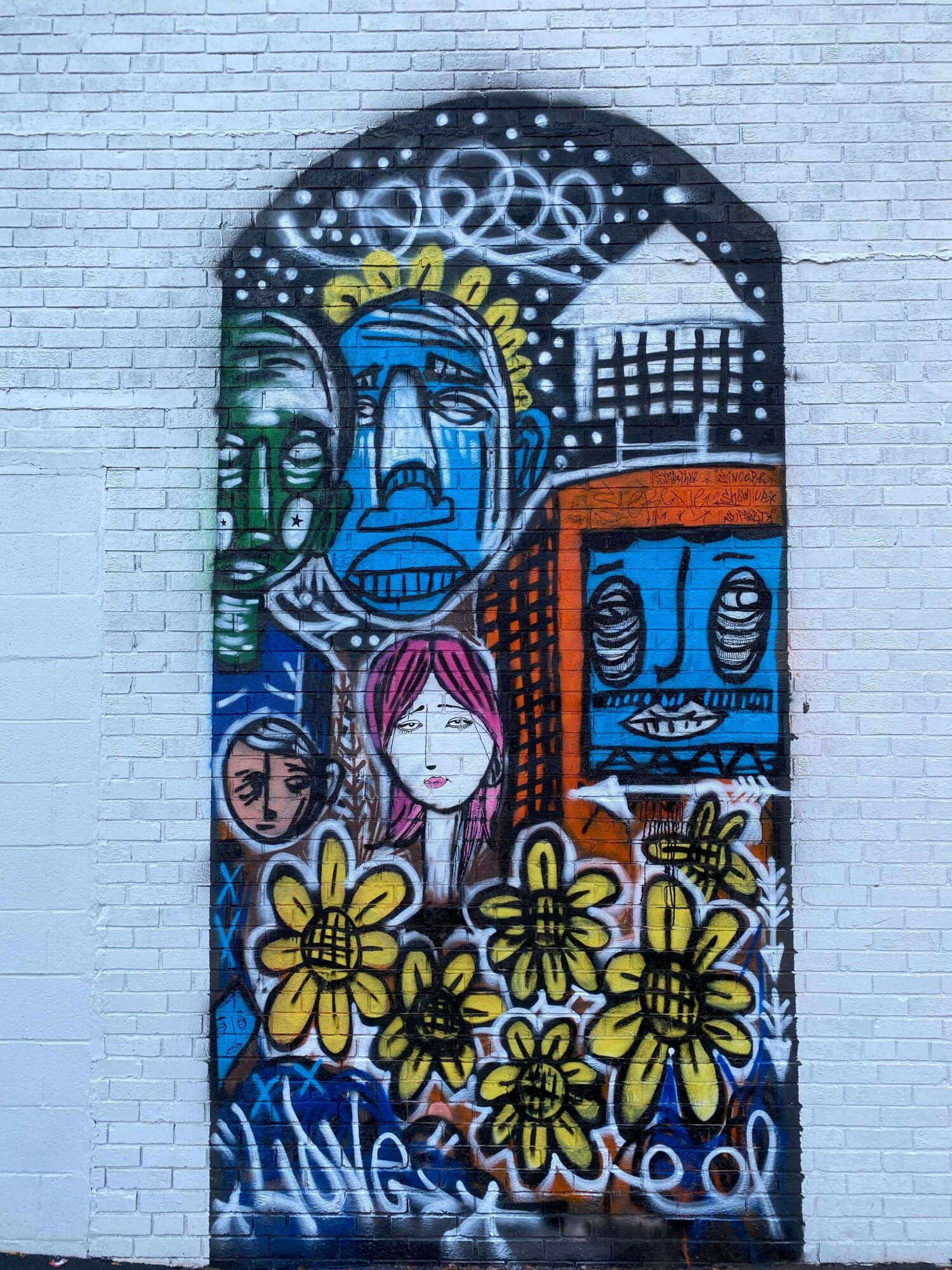Colorful graffiti mural with faces, flowers, and abstract patterns on a brick wall.
