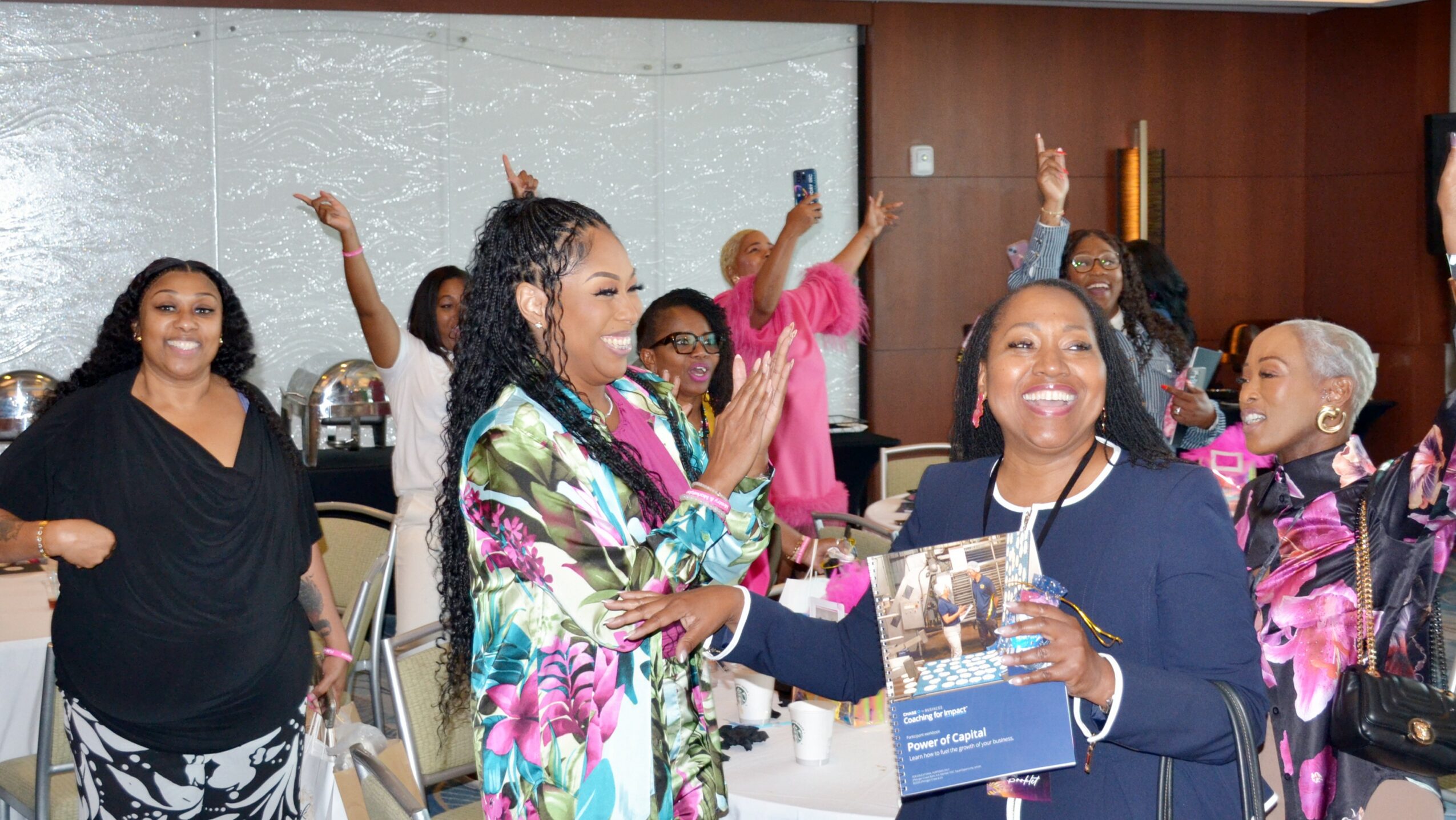 Group of women at a celebration, some smiling and holding a book, in a decorated indoor setting.