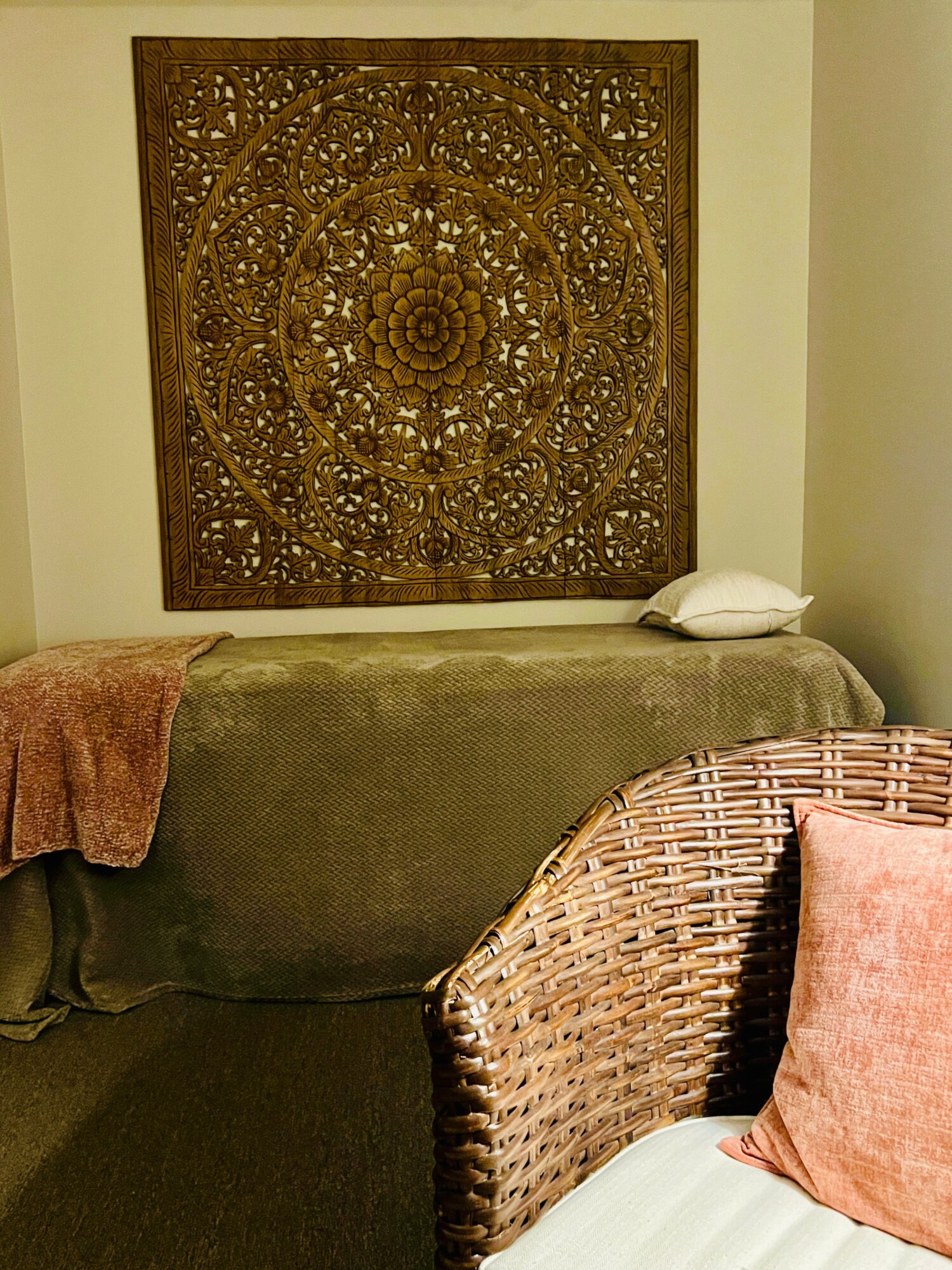 Decorative wooden wall art above a sofa with a pillow and blanket, wicker chair with a pillow in a cozy room.