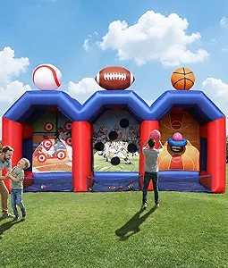 Children playing near a blue and red inflatable bounce house with sports balls on top, on a grassy field under a partly cloudy sky.