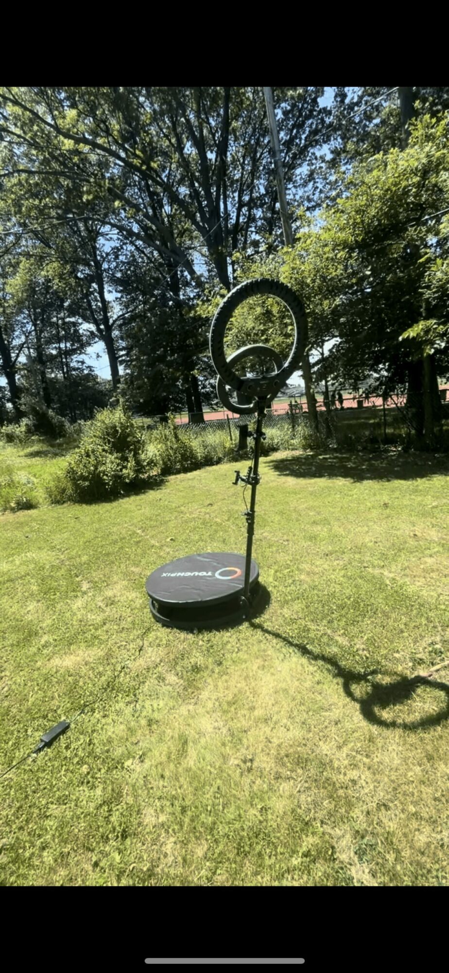 A robotic lawn mower on grass with a circular base and a tall pole with a ring at the top, outdoors.