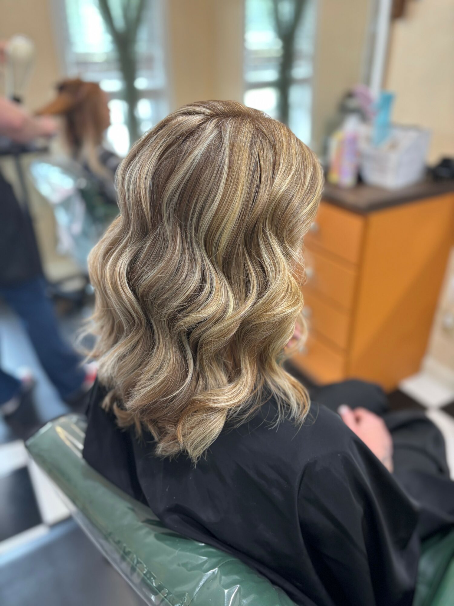 Side view of a woman with wavy, shoulder-length blonde hair in a salon chair.