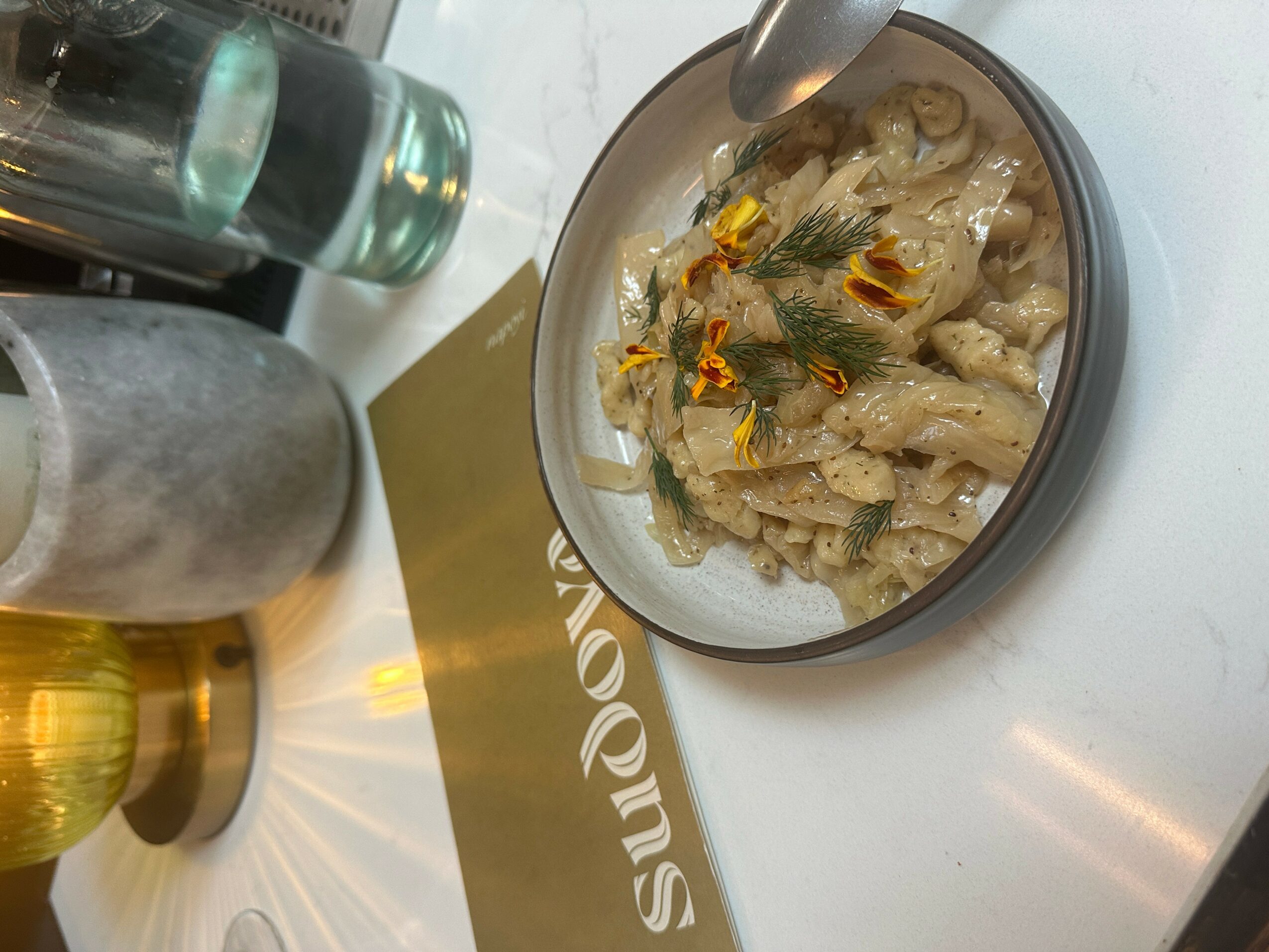 Bowl of pasta with creamy sauce and herbs on a white surface, with salt and pepper shakers nearby.