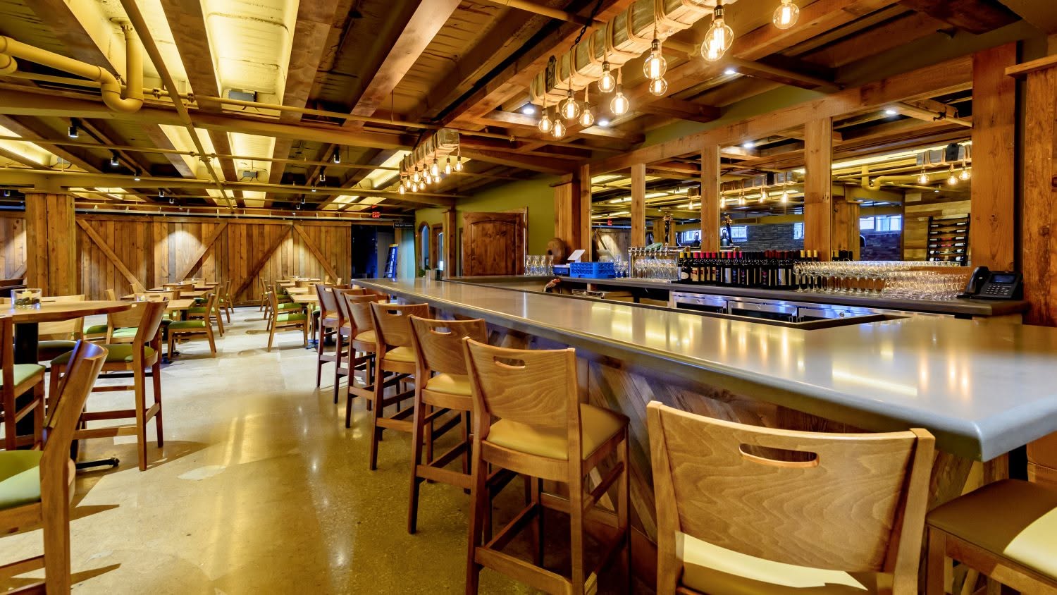Empty bar with wooden chairs and tables, illuminated by warm lighting, in a rustic-style interior.