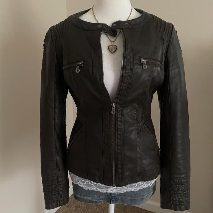 Black leather jacket with zippered pockets and quilted shoulder details, worn over a white lace-trimmed top, with a heart-shaped necklace.