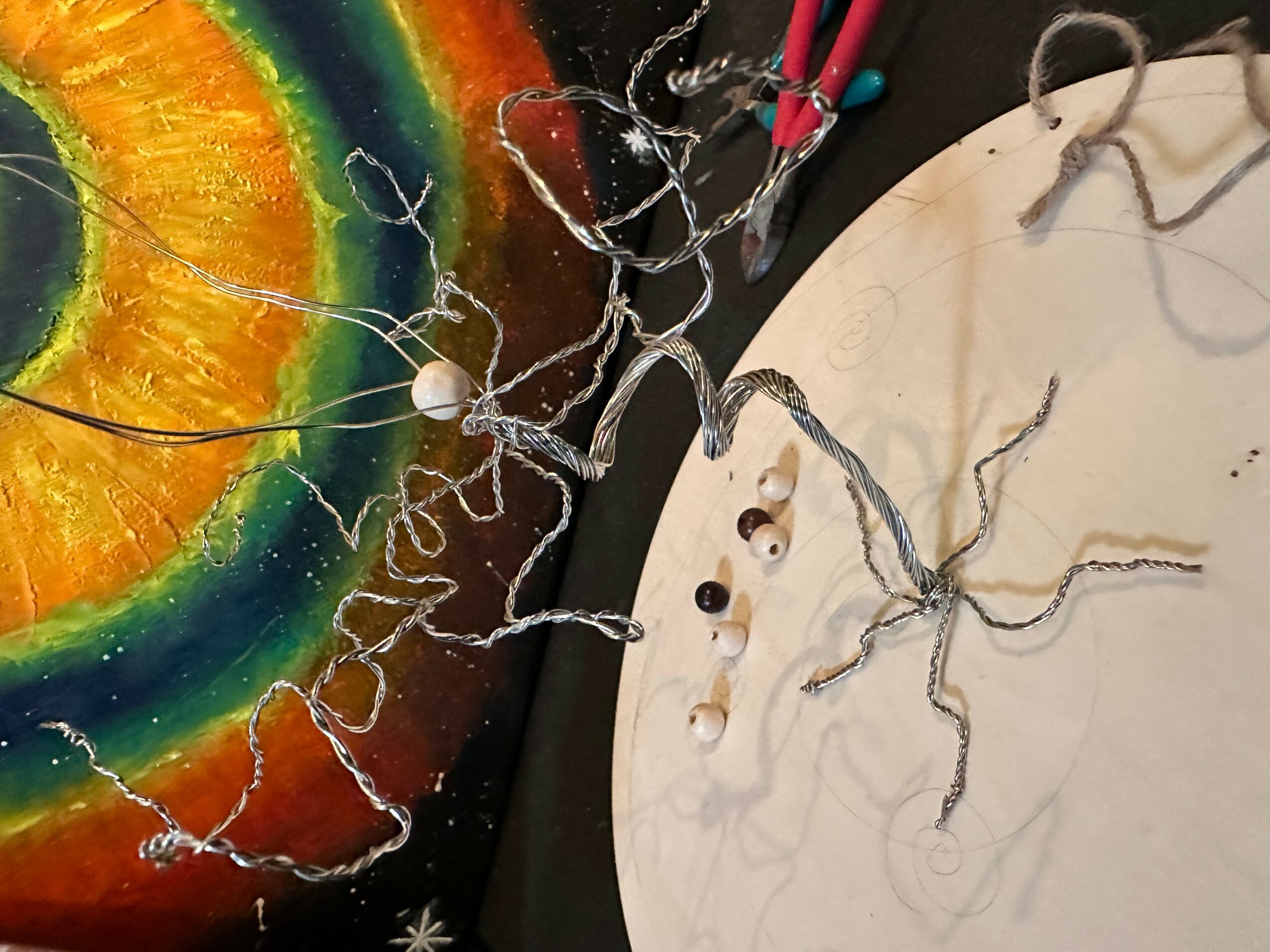 Colorful rainbow painting with tangled wires and small objects on a white surface.