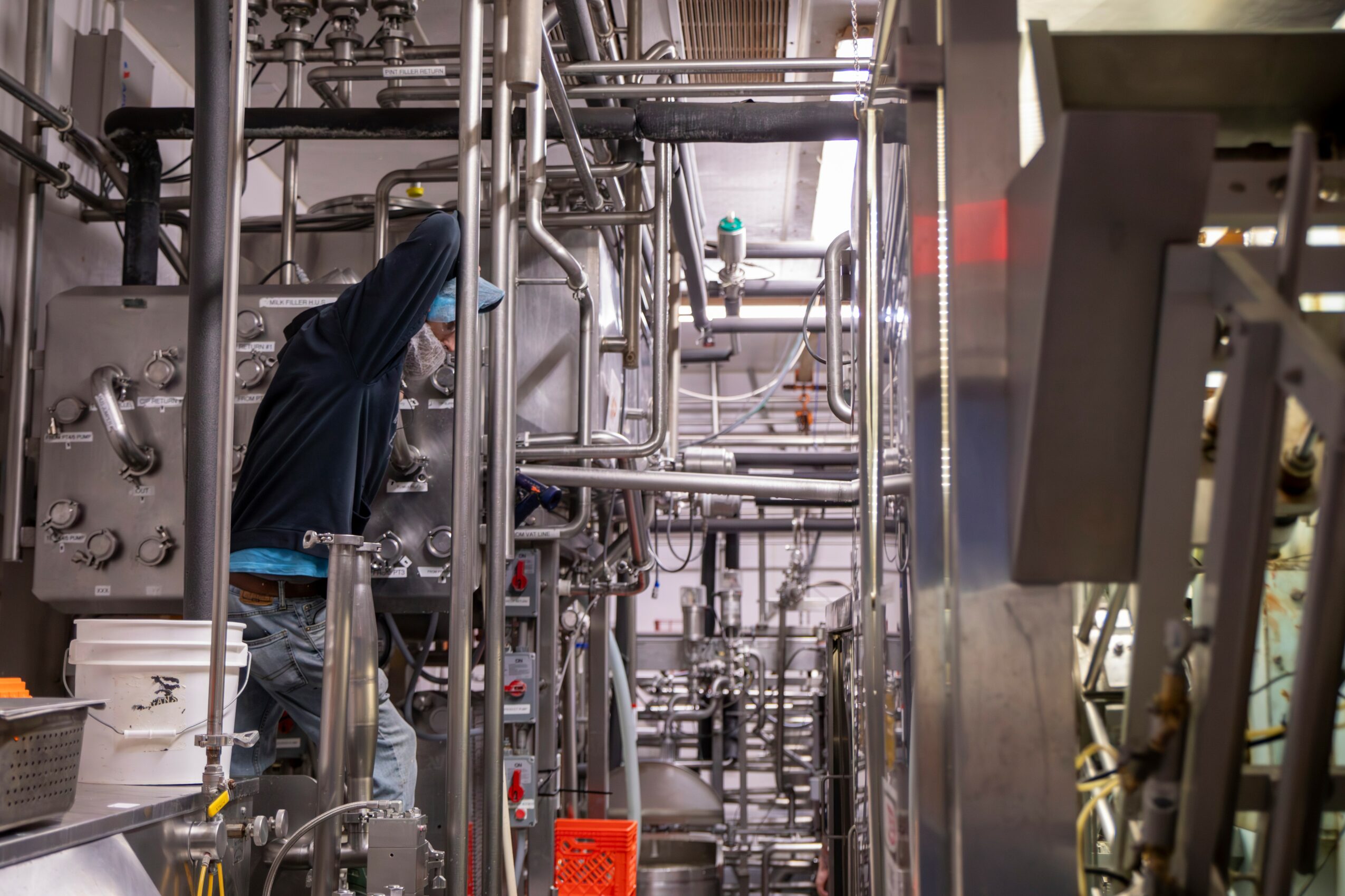 Person working with industrial pipes and machinery in a factory setting.