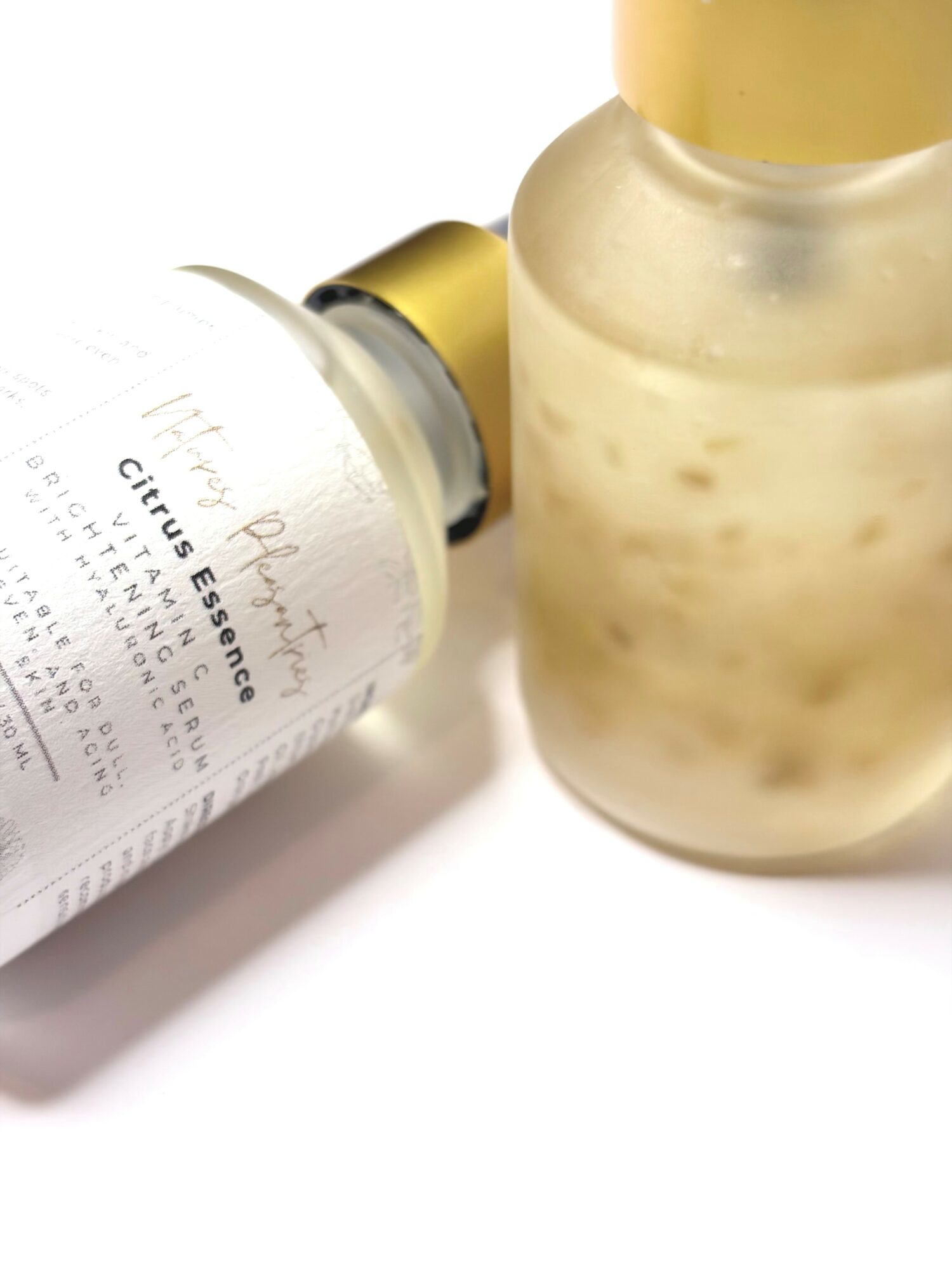 A skincare serum bottle with a gold cap and a jar with a cream or gel, both on a white surface.