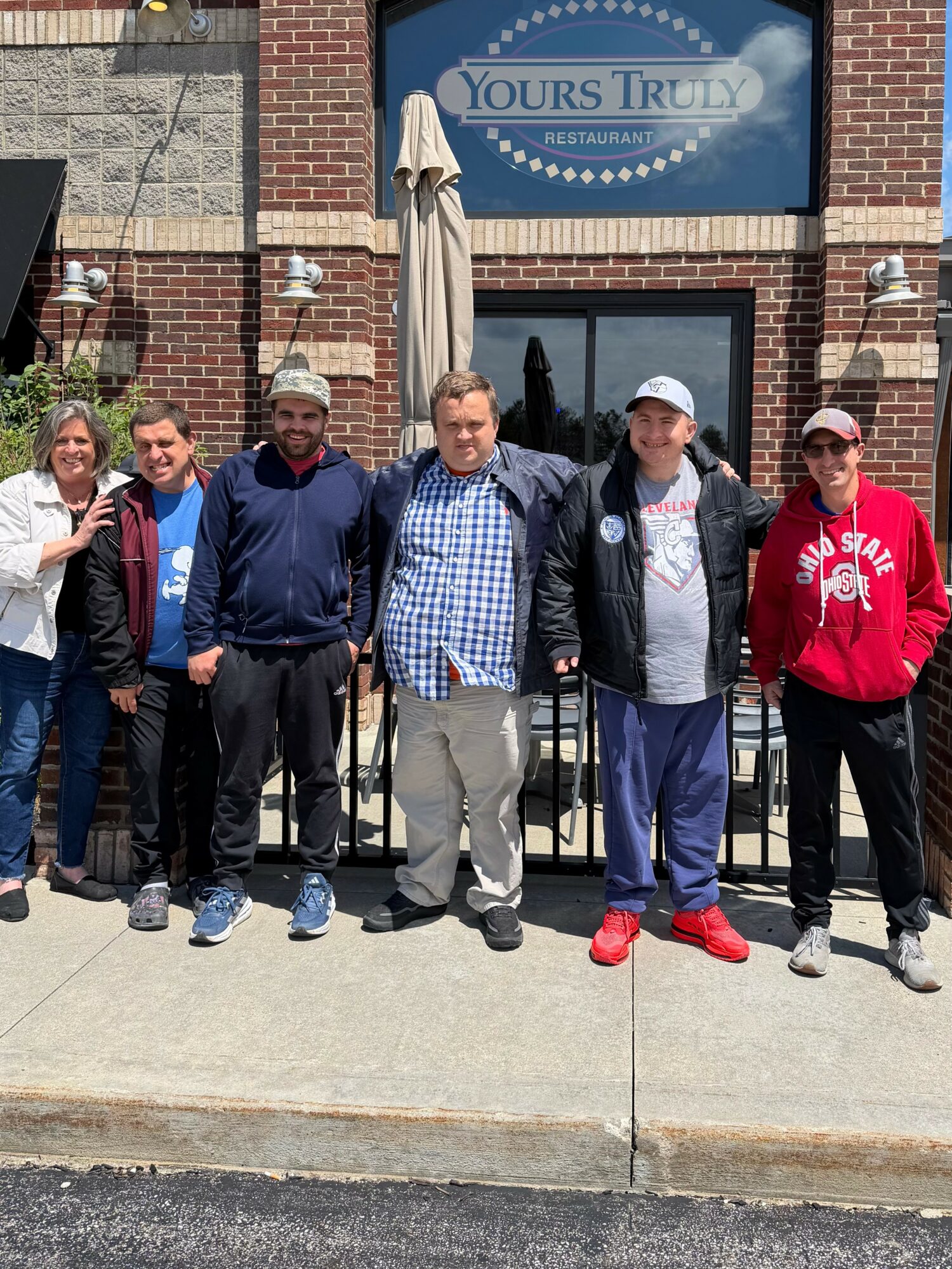 Group of six people standing outside a restaurant with a sign reading 'Yours Truly.'