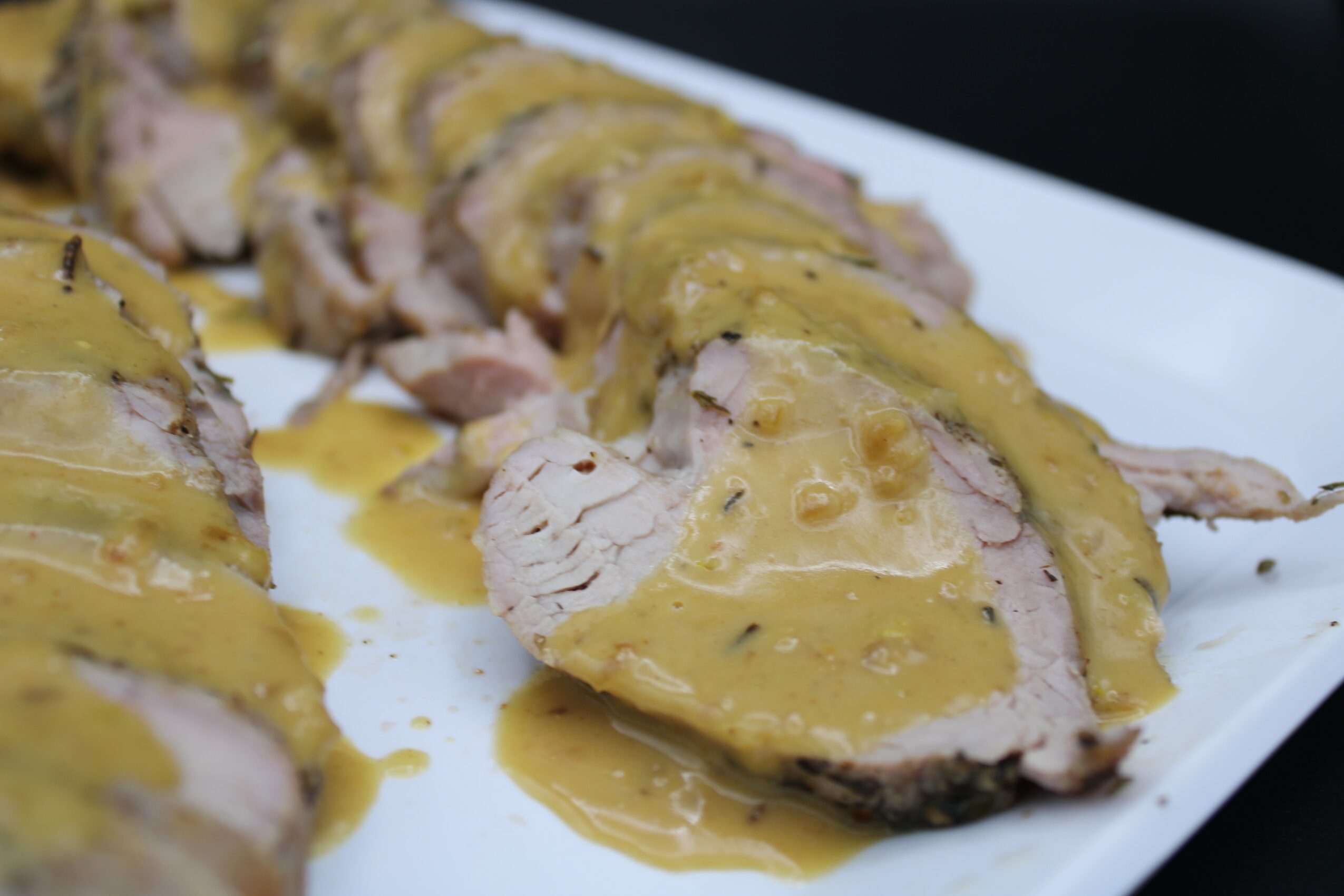 Sliced meat dish with yellow sauce on a white plate, close-up view.