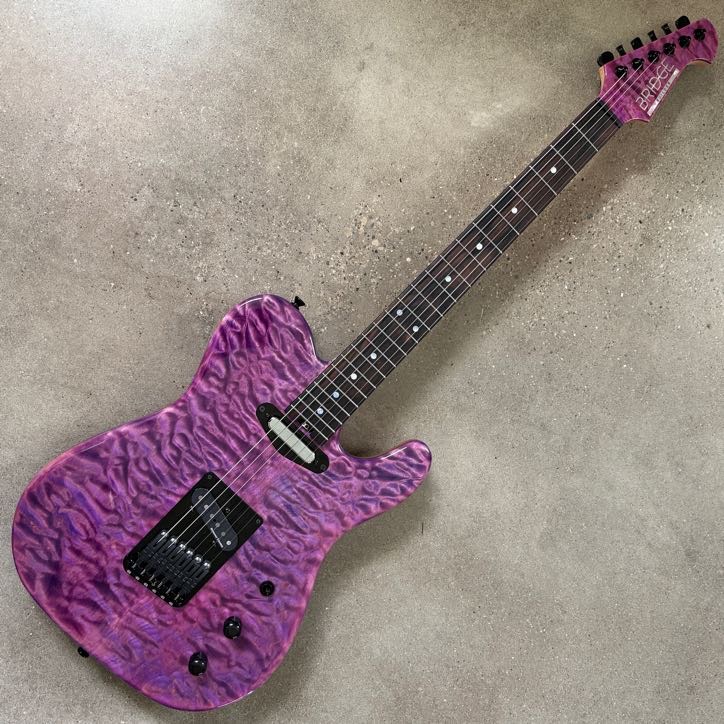 Electric guitar with a purple, textured body and black hardware, lying on a gray surface.