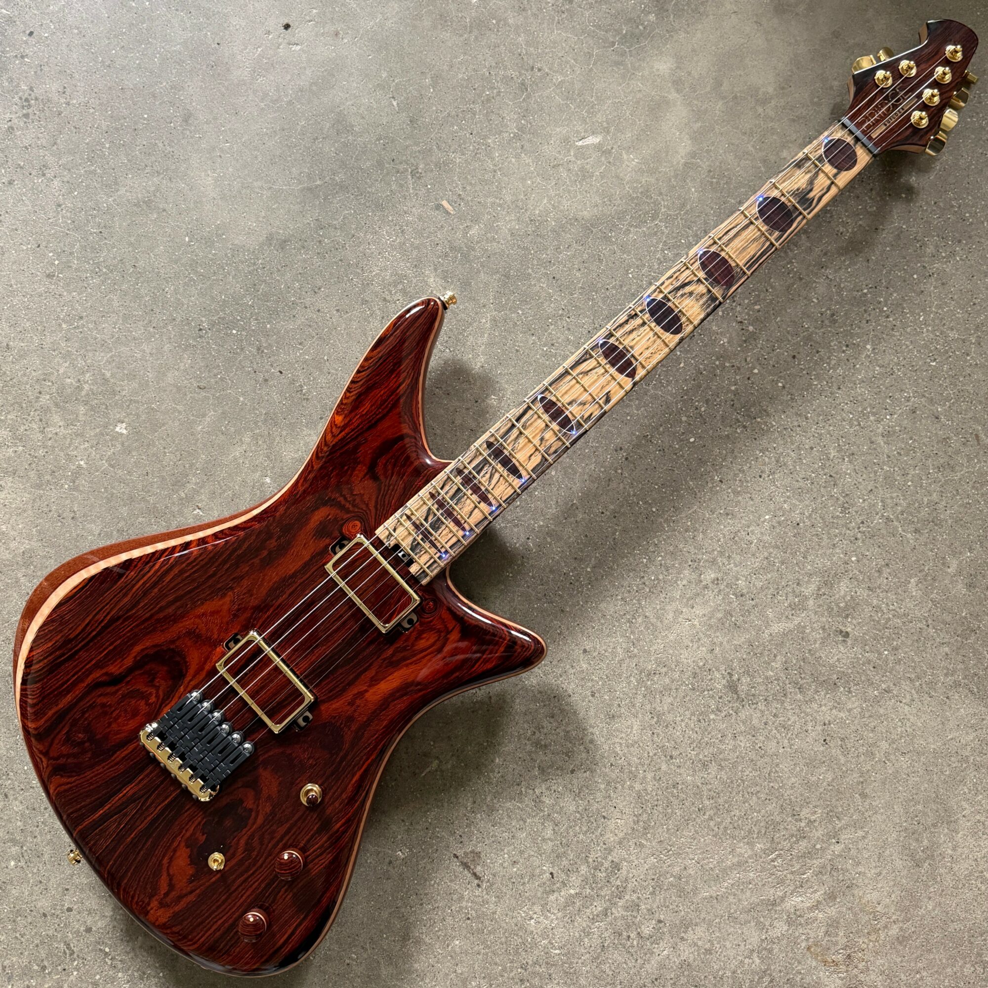 Electric guitar with a wooden finish, lying on a gray surface, with a long neck and six strings.